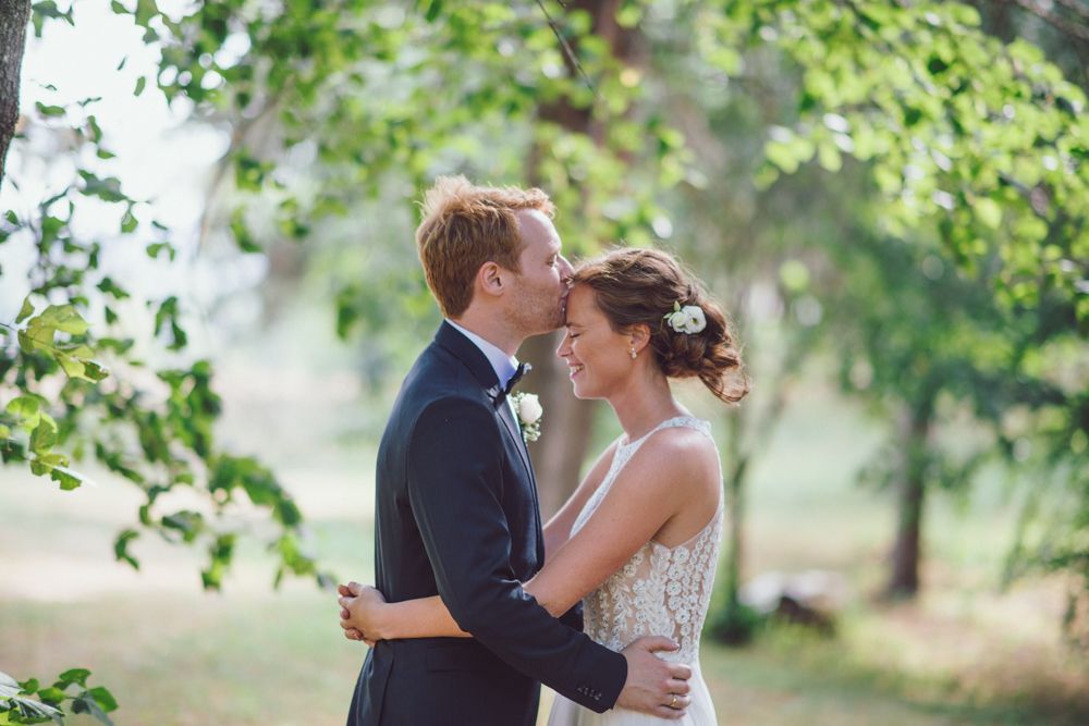 A tender embrace between newlyweds beneath green summer trees.