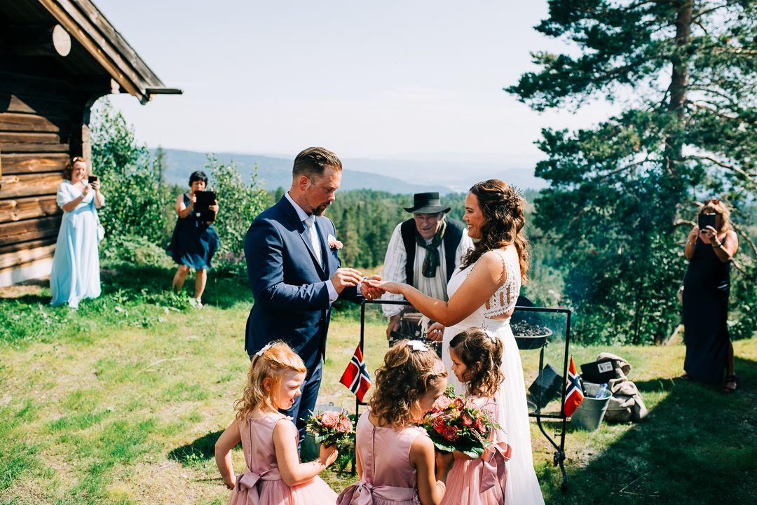 Wedding ceremony on mountainside with pine forest vista and rustic cabin in background.