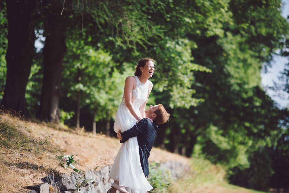 A romantic wedding moment captured on a wooded hillside with lush green trees in the background.