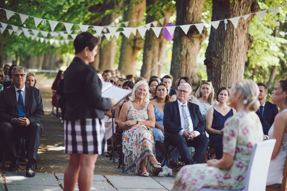 Outdoor wedding ceremony with guests seated beneath bunting decorations.