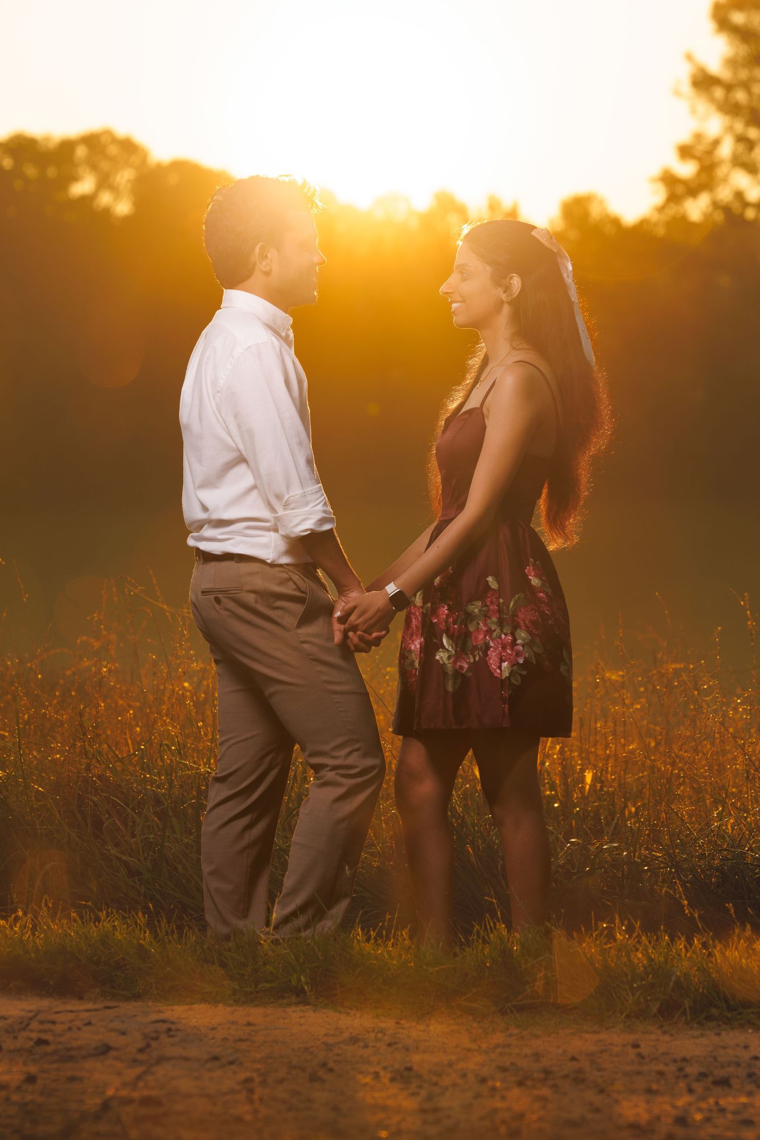 Couple standing together in a sunlit meadow during sunset with golden light filtering through.