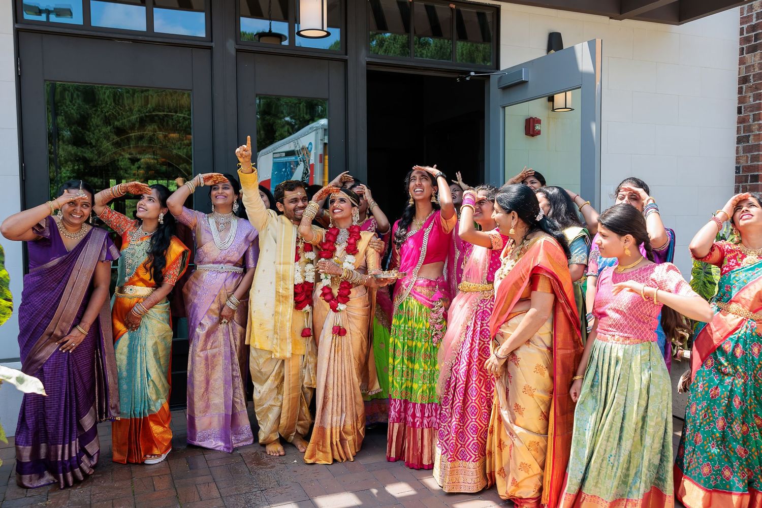Group of wedding guests in vibrant saris celebrating outside a building.