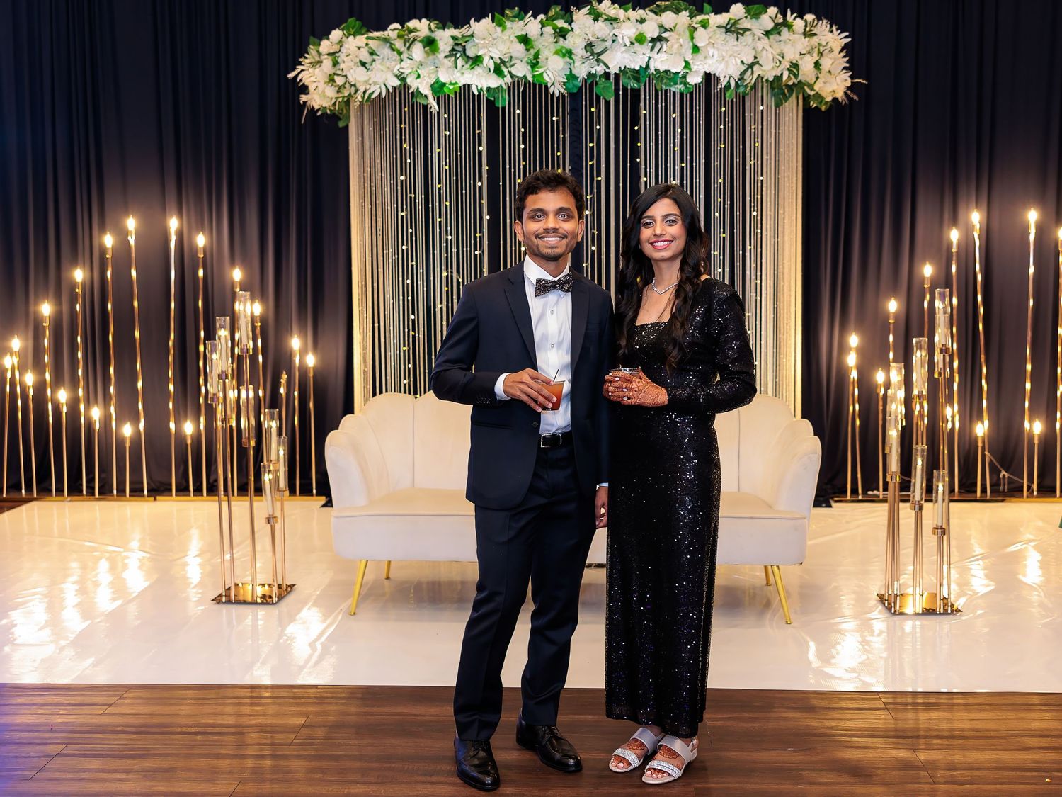 Elegant couple posing in front of floral arch backdrop with candlelit decor.