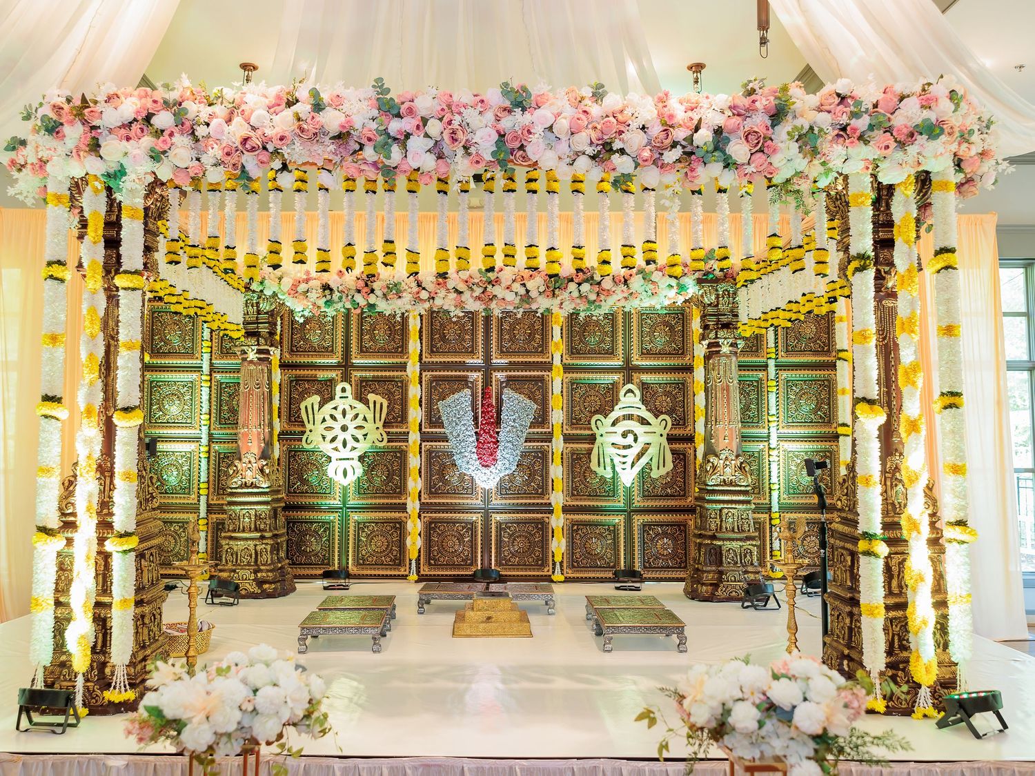 Traditional Hindu wedding mandap with floral garlands, bamboo pillars and intricate woodwork backdrop.