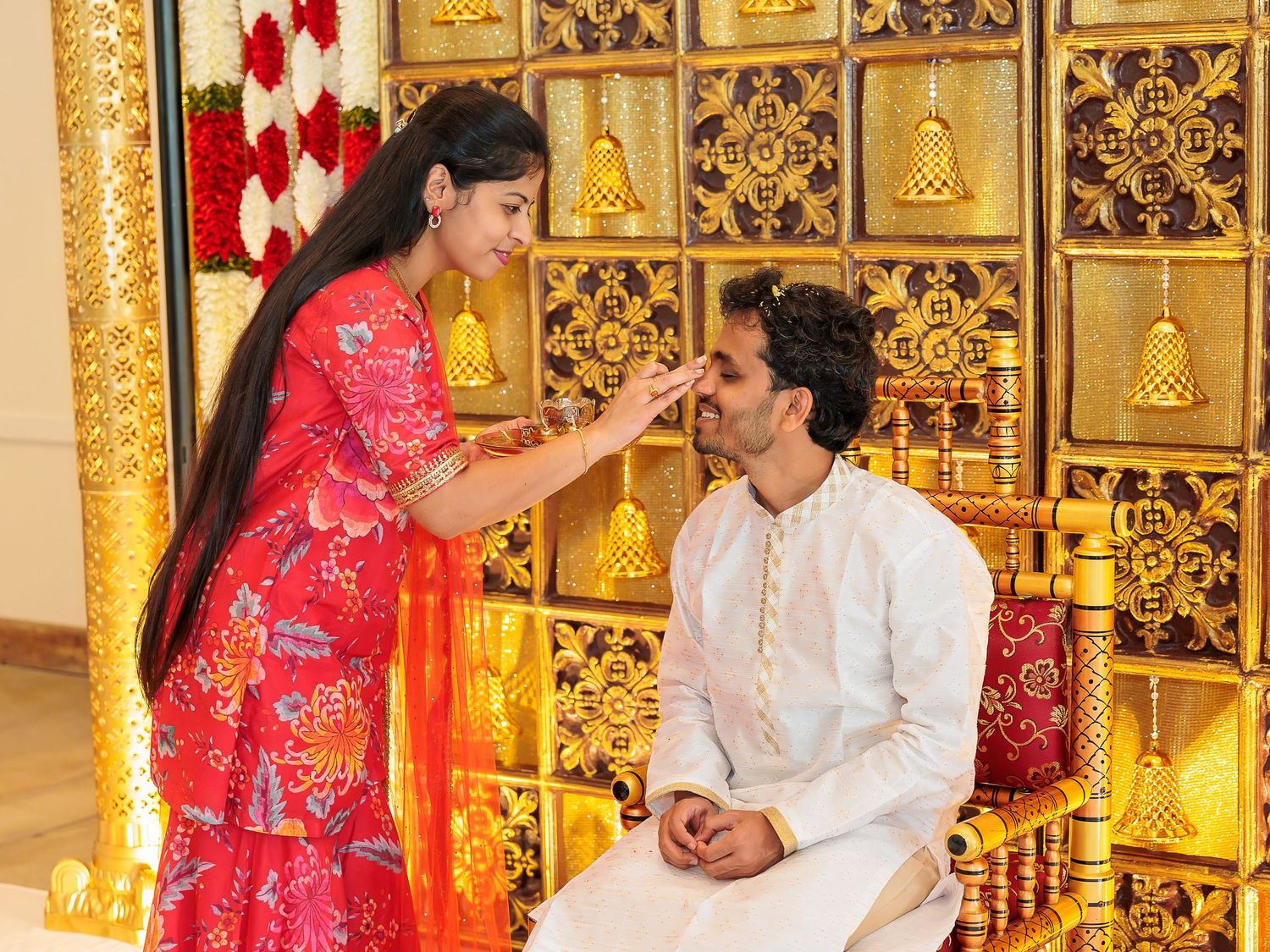 Traditional pre-wedding ceremony with ornate golden bell backdrop and decorative elements.
