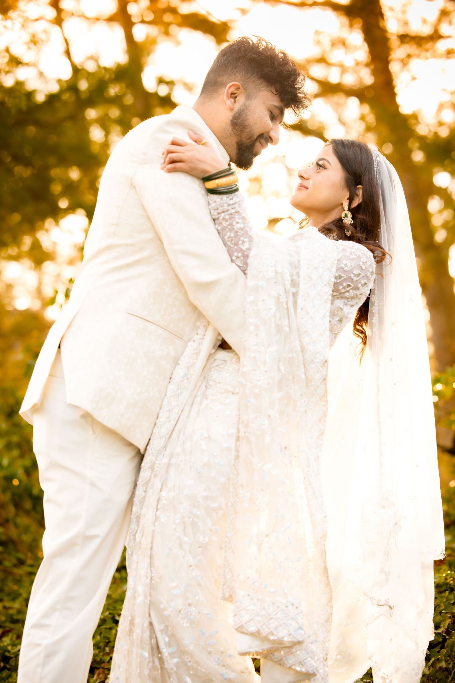 An intimate wedding portrait against a golden sunset backdrop with the couple in matching white outfits.