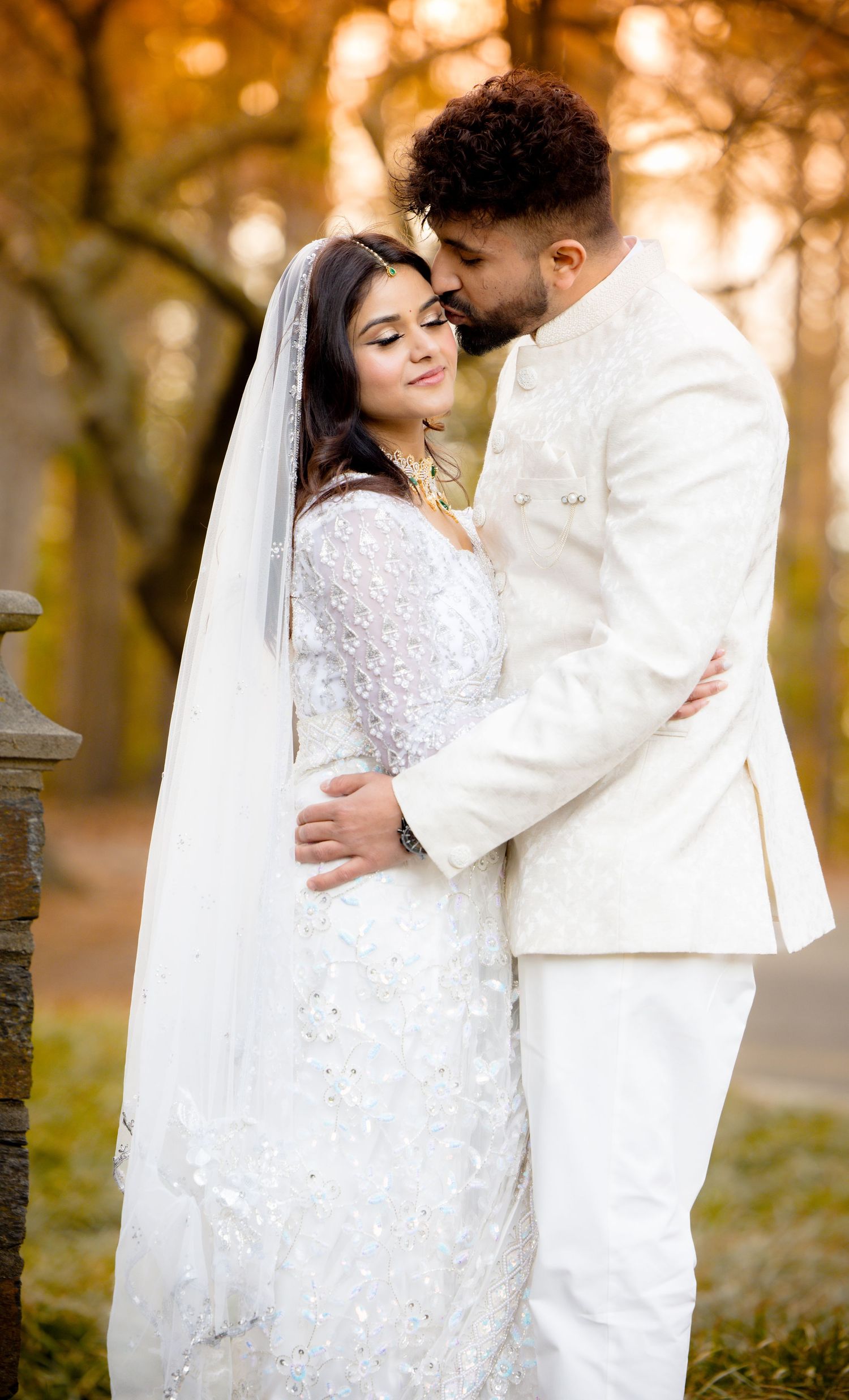 A romantic autumn wedding portrait with a couple in white embracing outdoors.