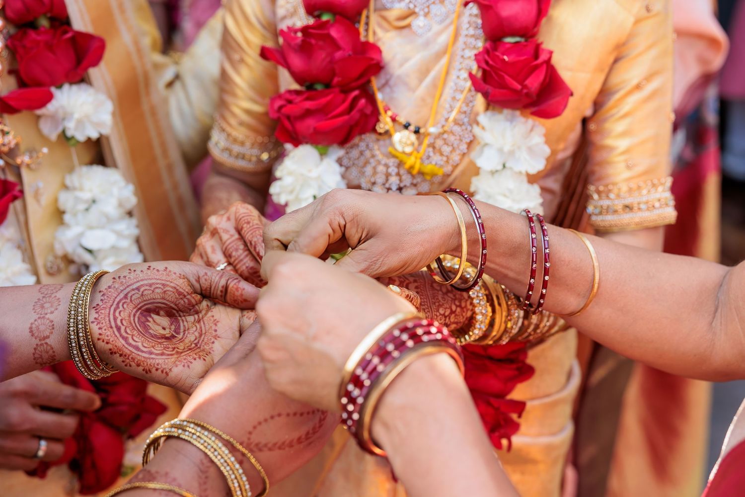 Close-up of hands exchanging jewelry and bangles during traditional Indian wedding ceremony.