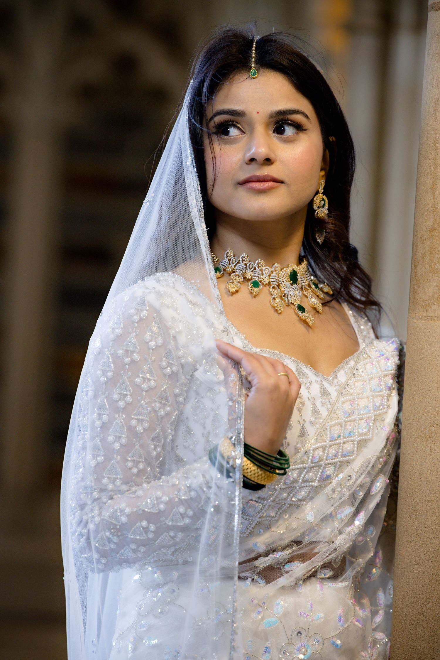 A bride in white traditional South Asian attire wearing crystal jewelry and a delicate veil.