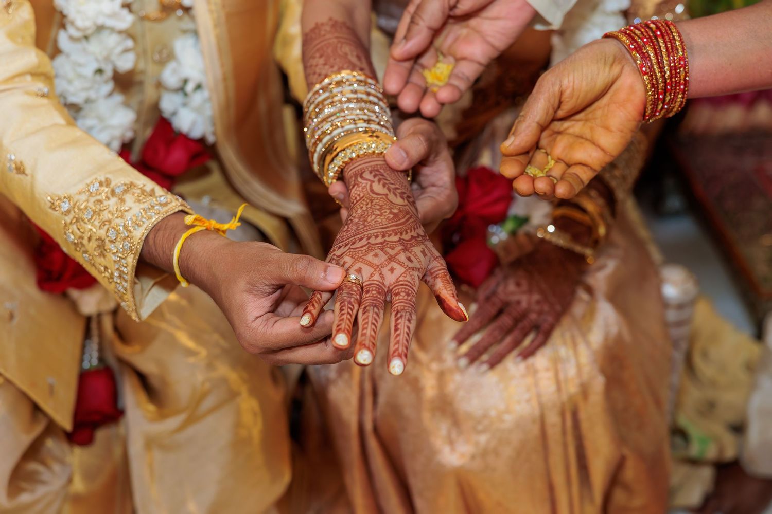 Close-up of hands adorned with henna and jewelry during an Indian wedding ceremony.