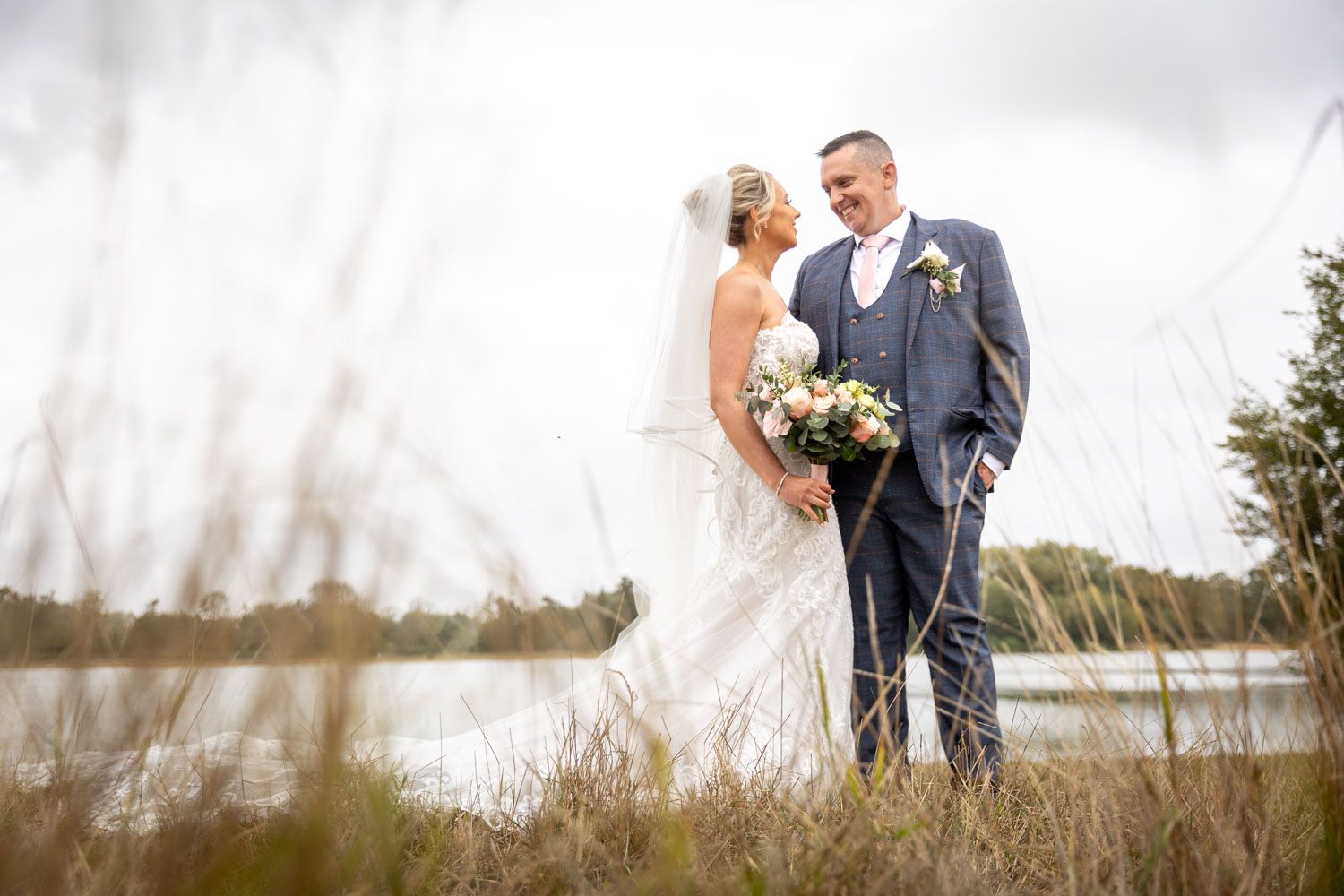 Romantic couple shares intimate moments in a grassy field with scenic water views on their wedding day at Testwood lakes