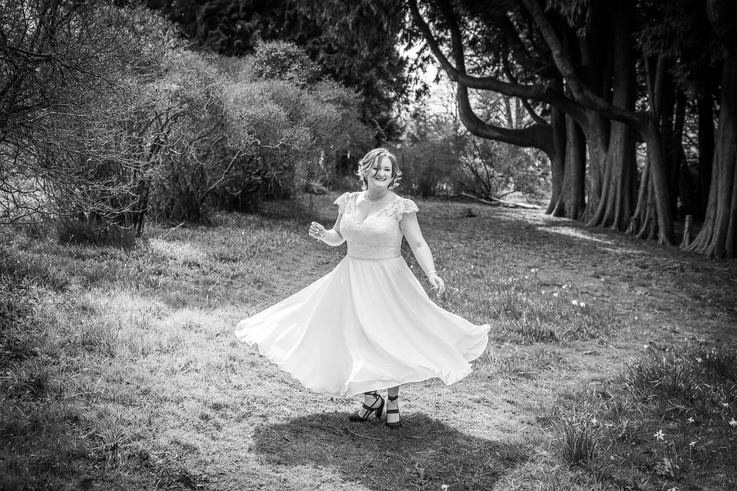 A whimsical black and white photo of a twirling wedding dress in a tree-lined meadow.