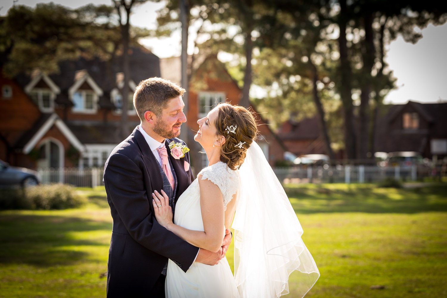 A loving couple shares a romantic moment during their wedding in a sunlit garden setting with a house in the background.