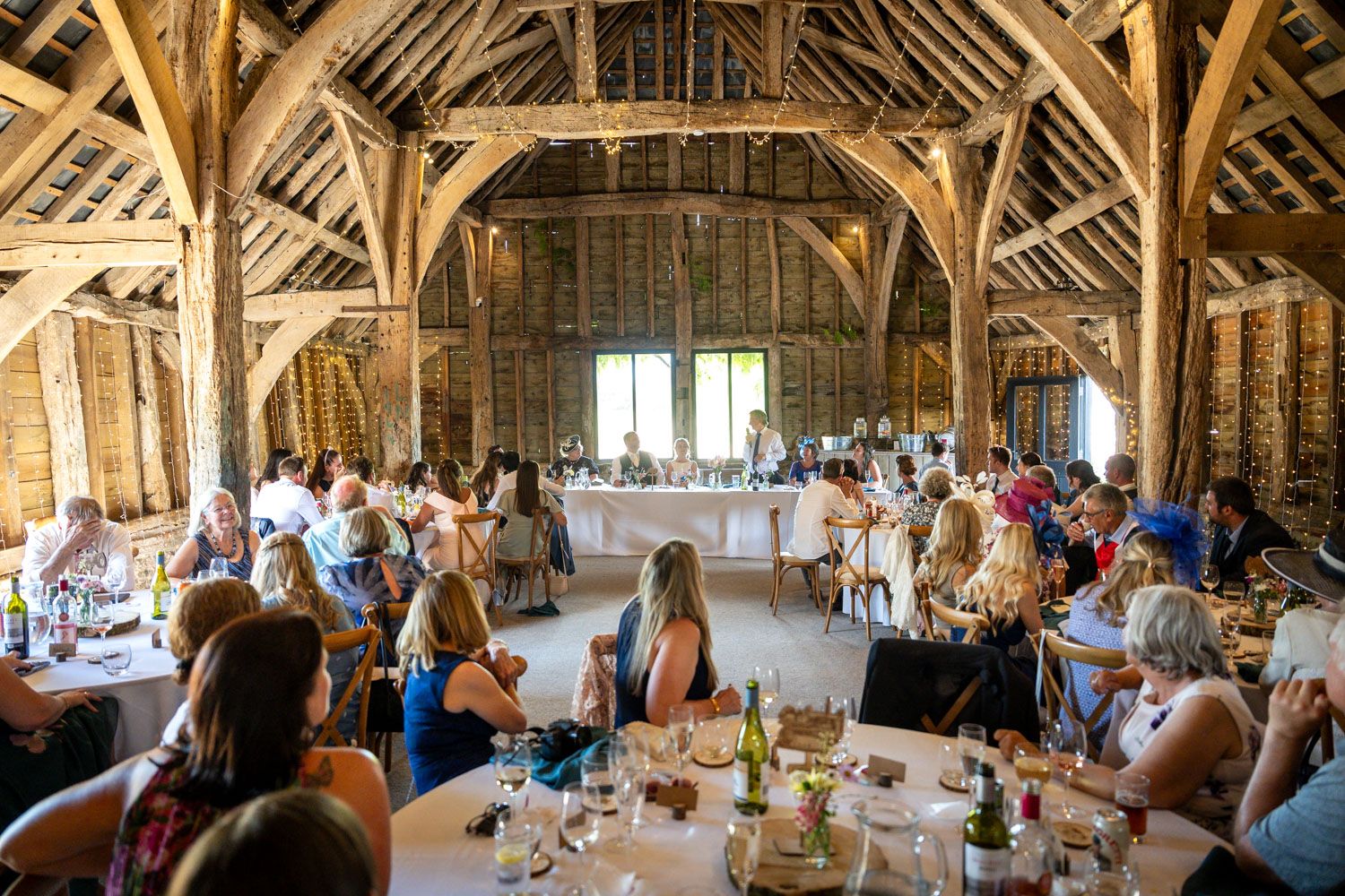 Guests dining in a rustic barn venue with exposed wooden beams during a wedding reception.
