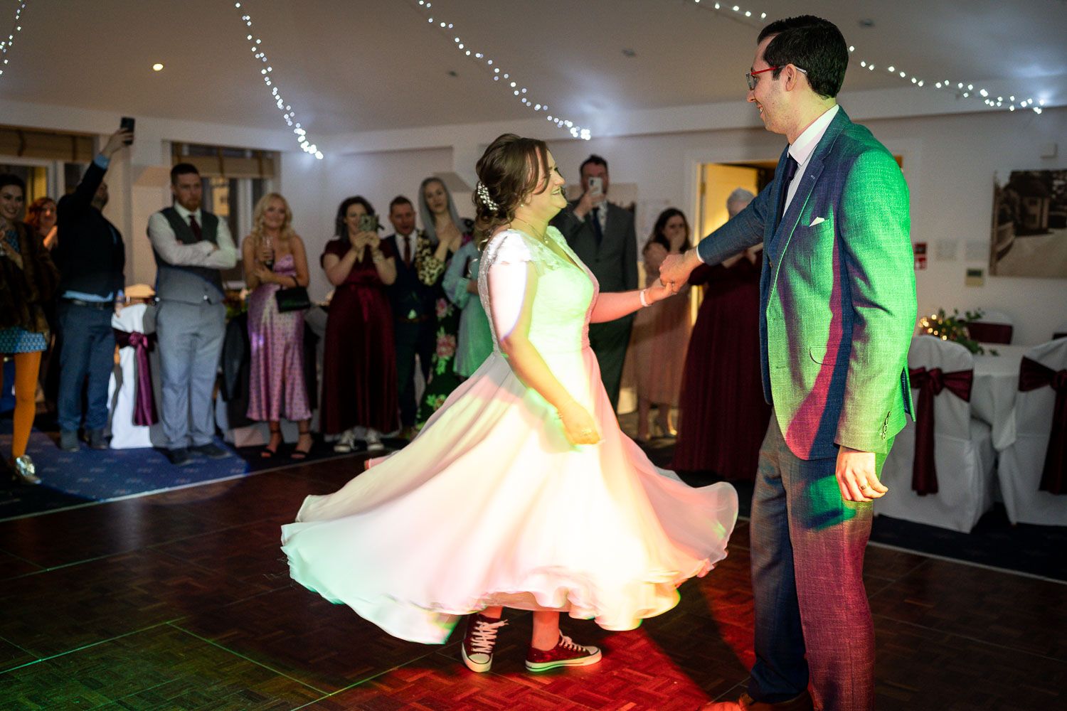 Two dancers performing their first dance at a wedding reception with guests watching in the background beneath twinkling lights.