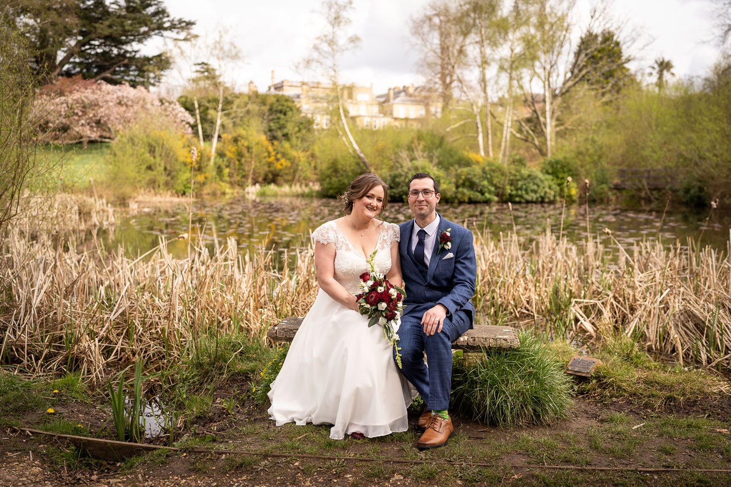 A couple poses together on a rustic bench surrounded by autumn meadow grass and trees at an outdoor venue.