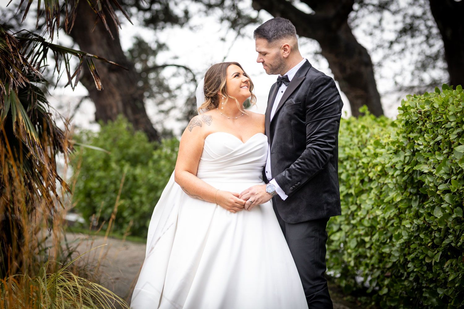A romantic outdoor wedding portrait of a couple embracing on a garden path surrounded by lush greenery.