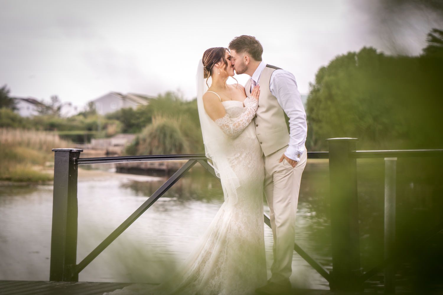 A romantic moment between a couple in white at a lakeside wooden dock in soft, dreamy lighting.