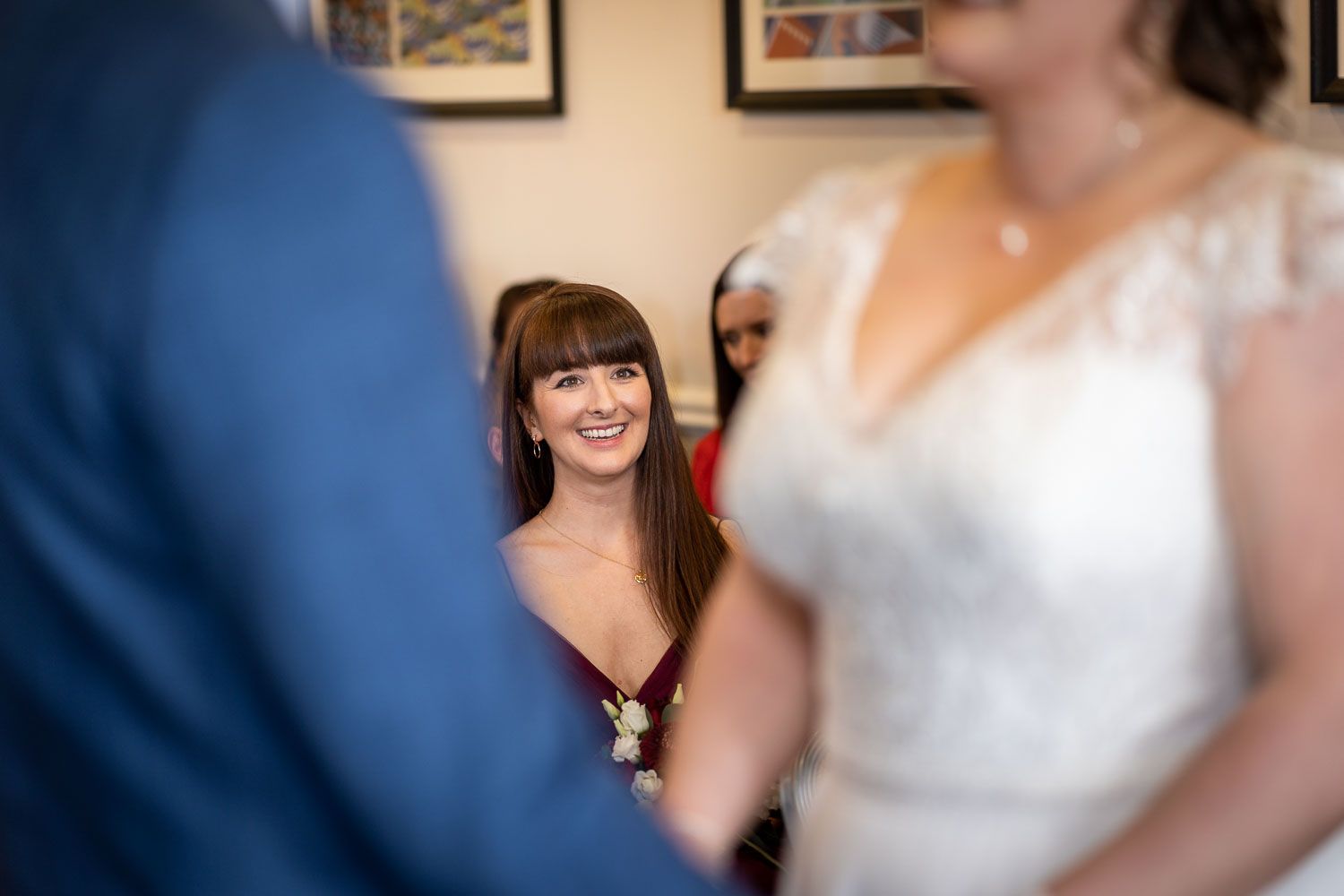 Wedding guests smile and share a joyful moment during the ceremony in an indoor venue with framed artwork on the wall.