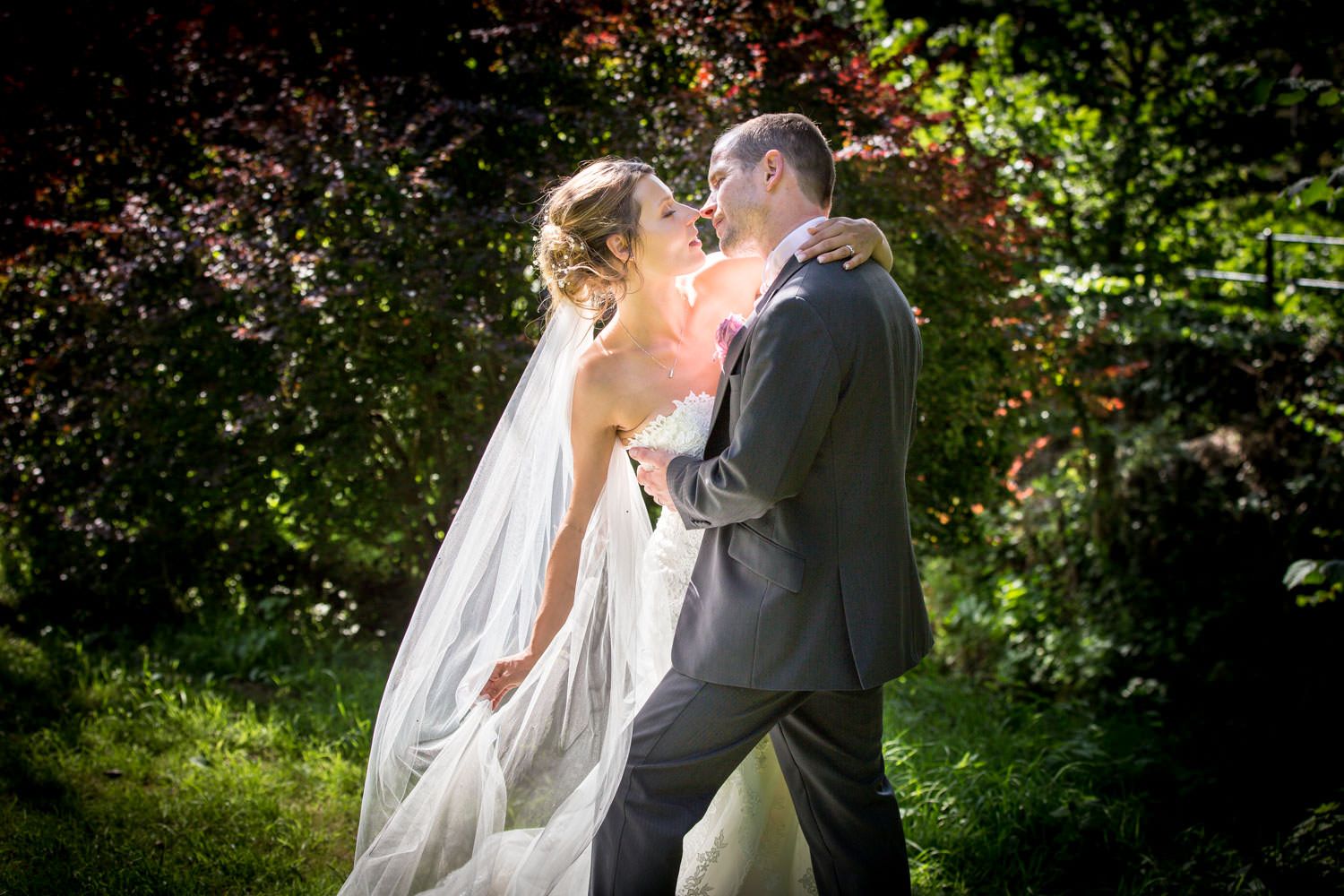 A romantic wedding moment captured in a lush garden setting with sunlight filtering through the trees.