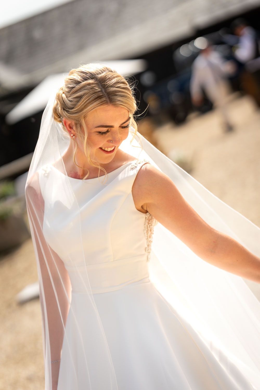 Smiling bride in white gown and flowing veil twirling outdoors on sunny wedding day.