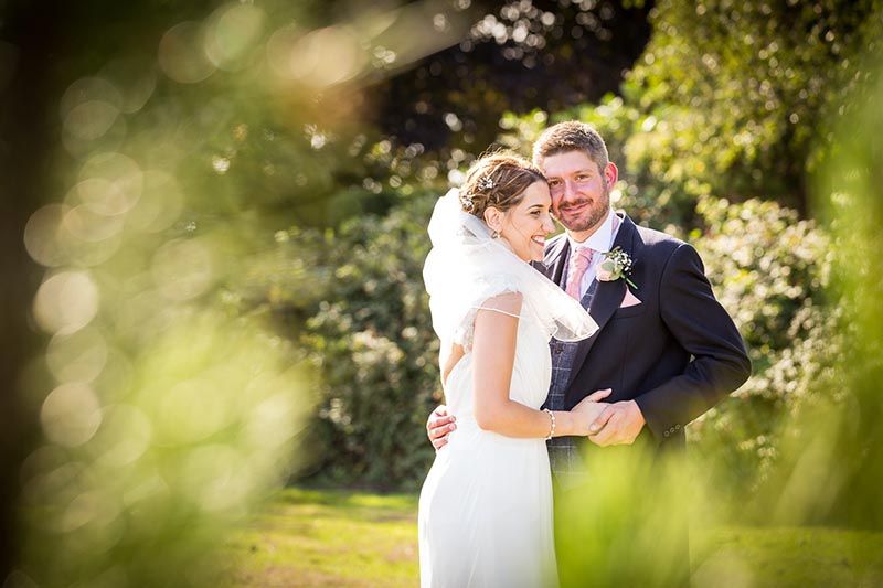 A tender wedding moment captured in a garden setting with soft bokeh lighting and lush greenery in the background.