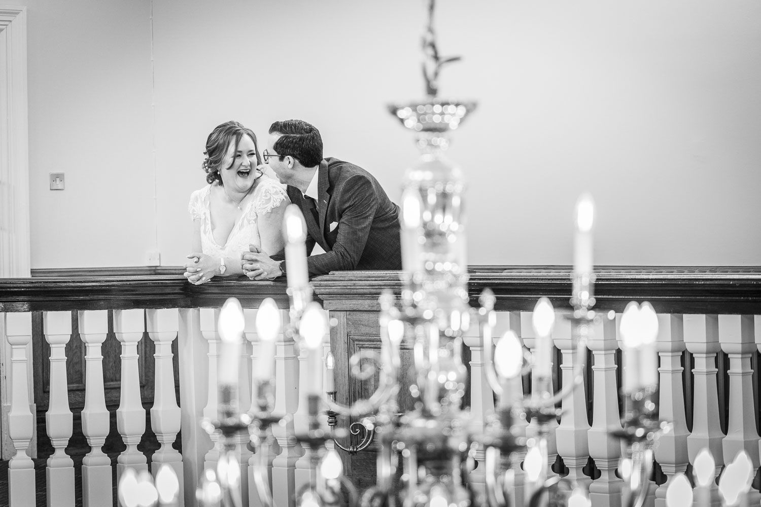 A romantic black and white wedding moment captured behind an elegant crystal chandelier with glowing candles.
