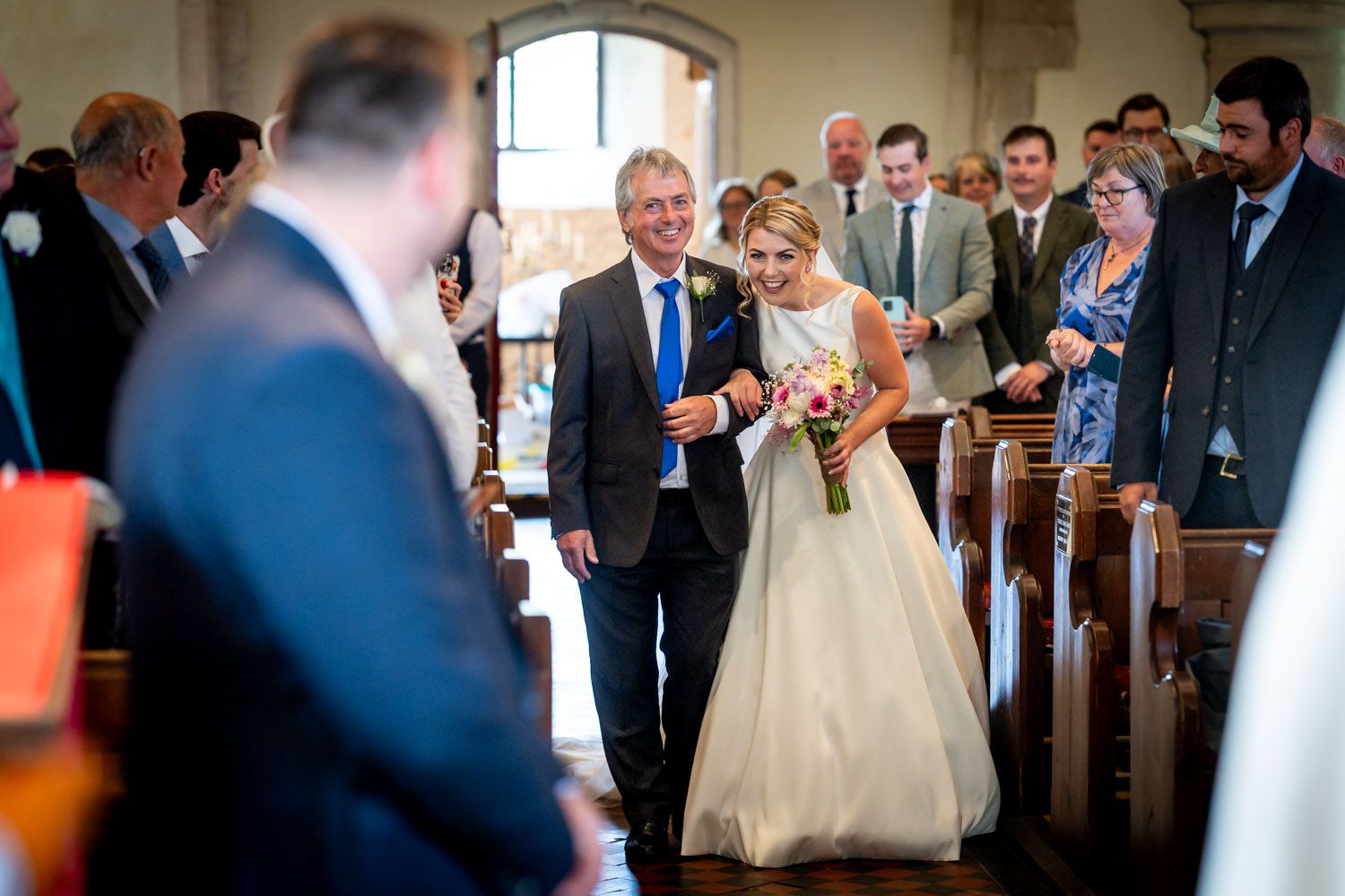 A beaming bride walks down the church aisle with her father during a traditional wedding ceremony.