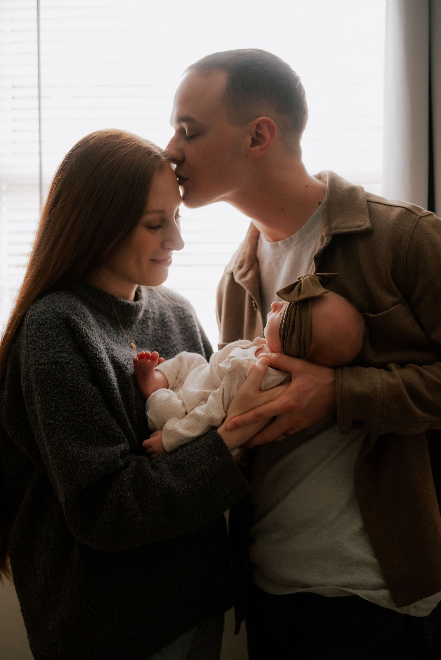 An intimate indoor portrait of parents cradling their newborn baby.