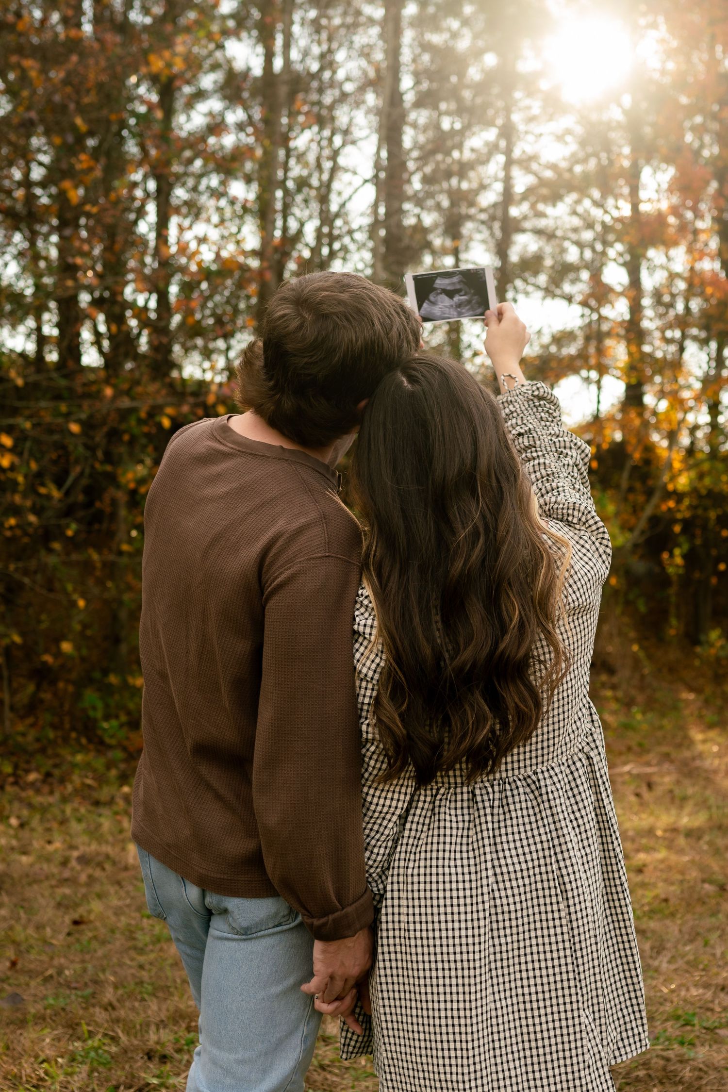 A couple embraces while walking together at sunset with autumn trees in the background.