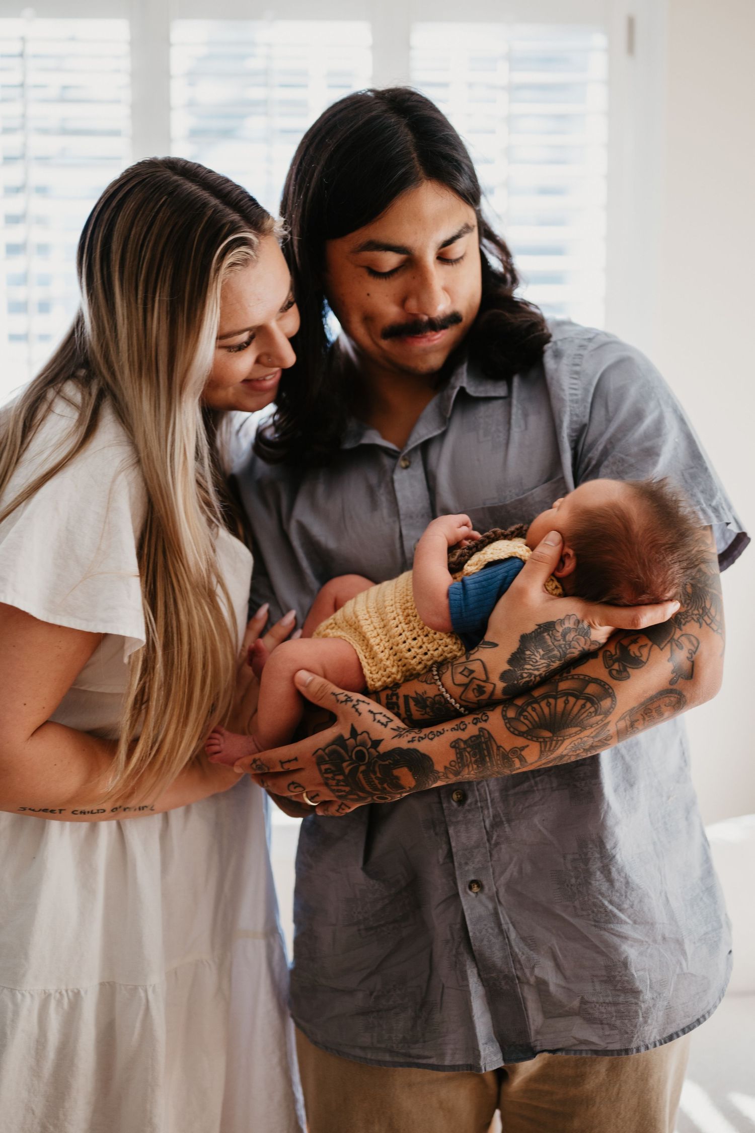 Couple sharing intimate moment while holding their newborn in sunlit living room.