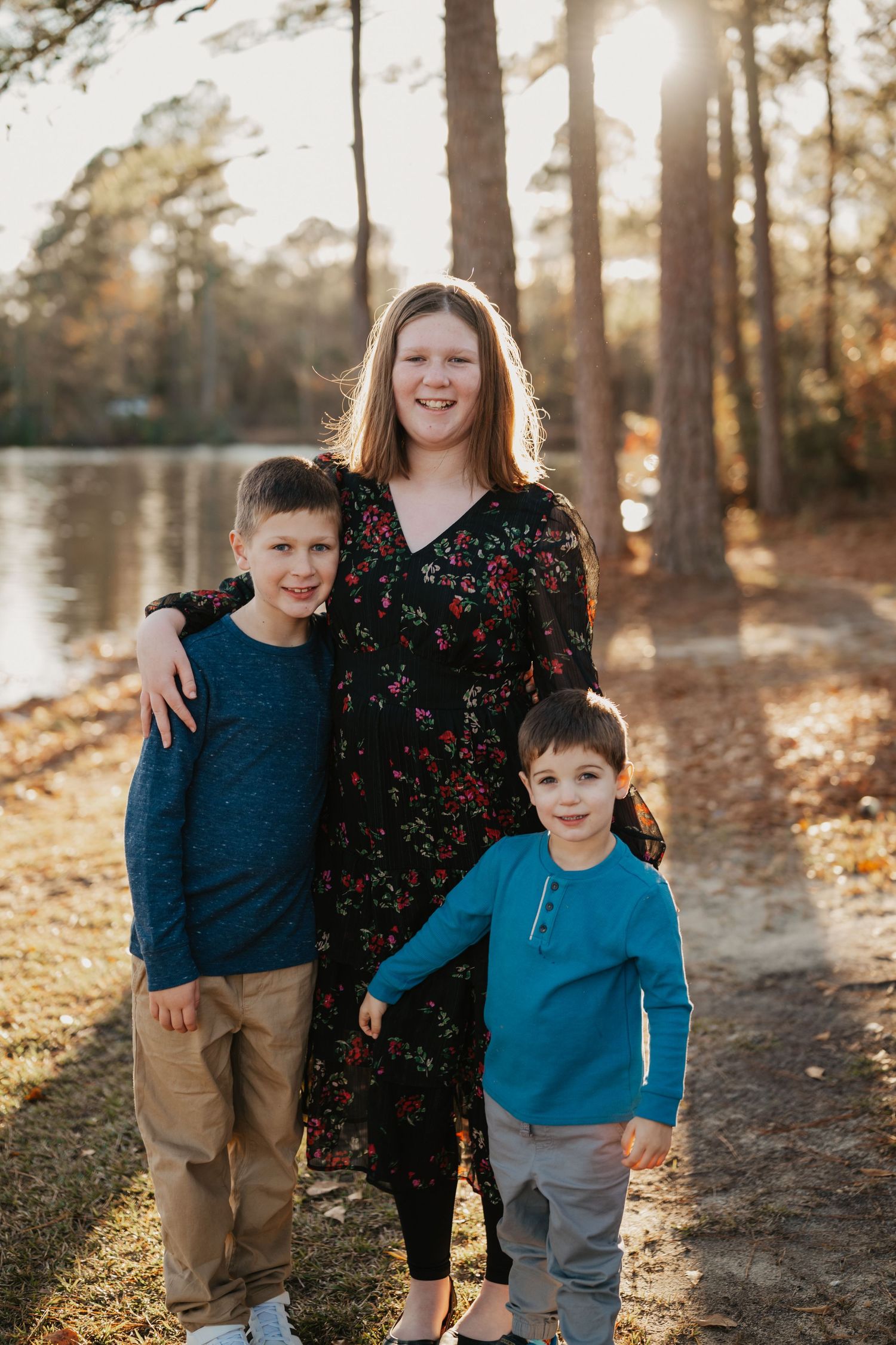 Portrait of parent with two children standing by lake during sunset.