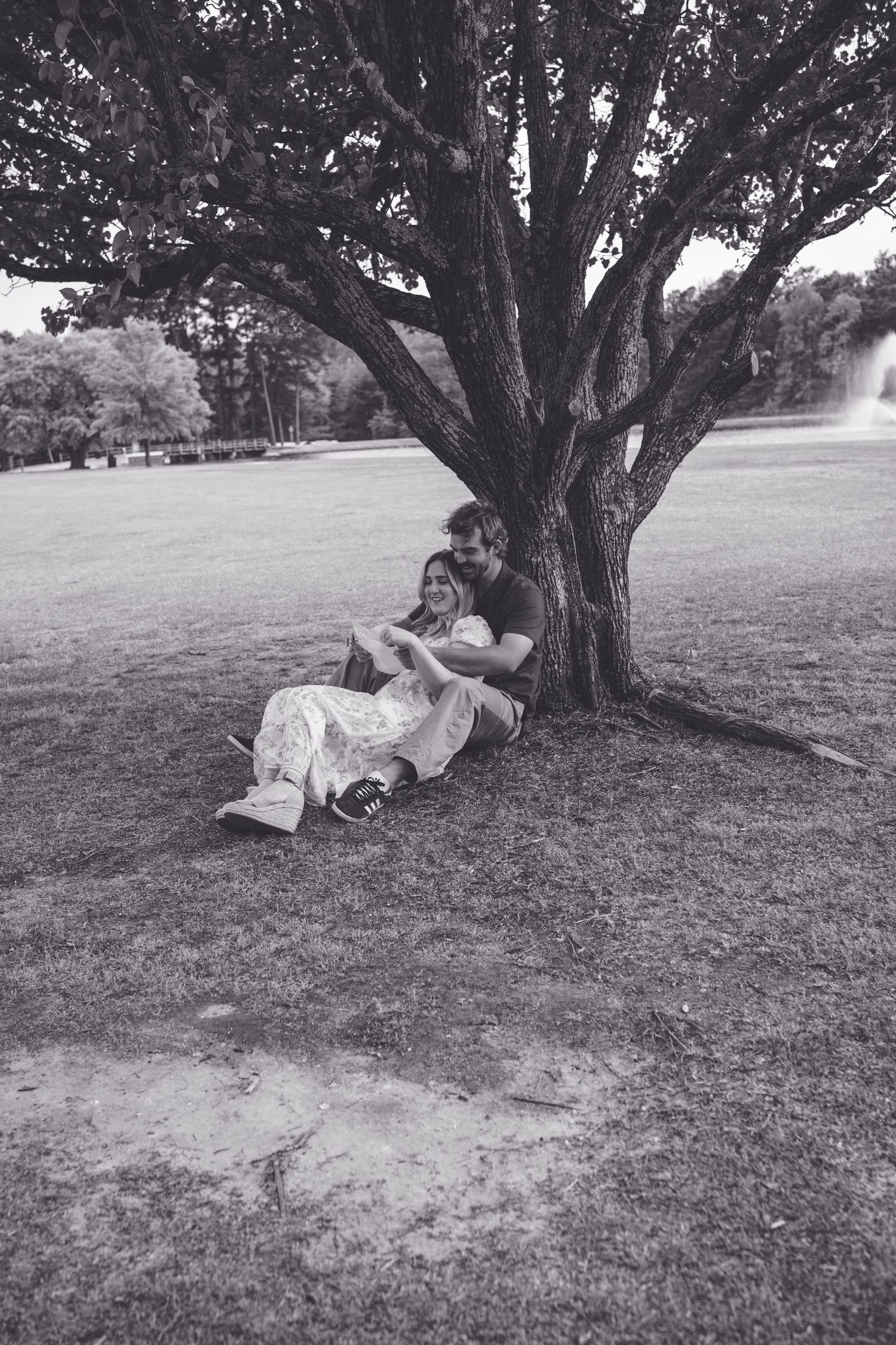 Couple sitting together under a large tree in a park, sharing a tender moment in black and white photography.