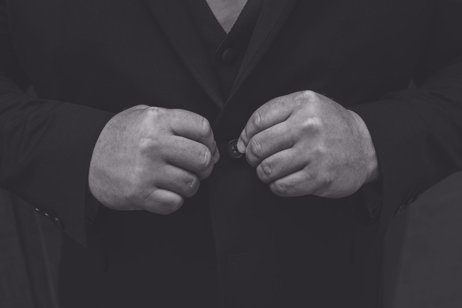 Black and white photo of a man in a suit adjusting his jacket with both hands.