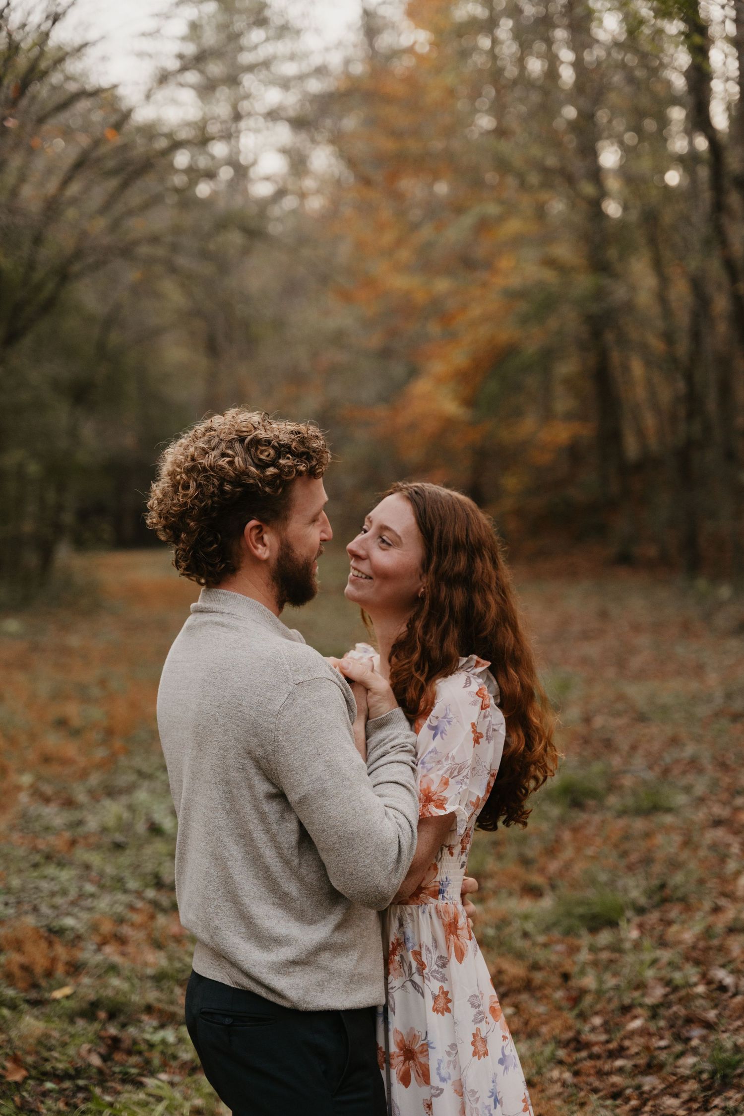 A couple embraces intimately in a wooded autumn setting with fallen leaves on the ground. Southern pines, NC