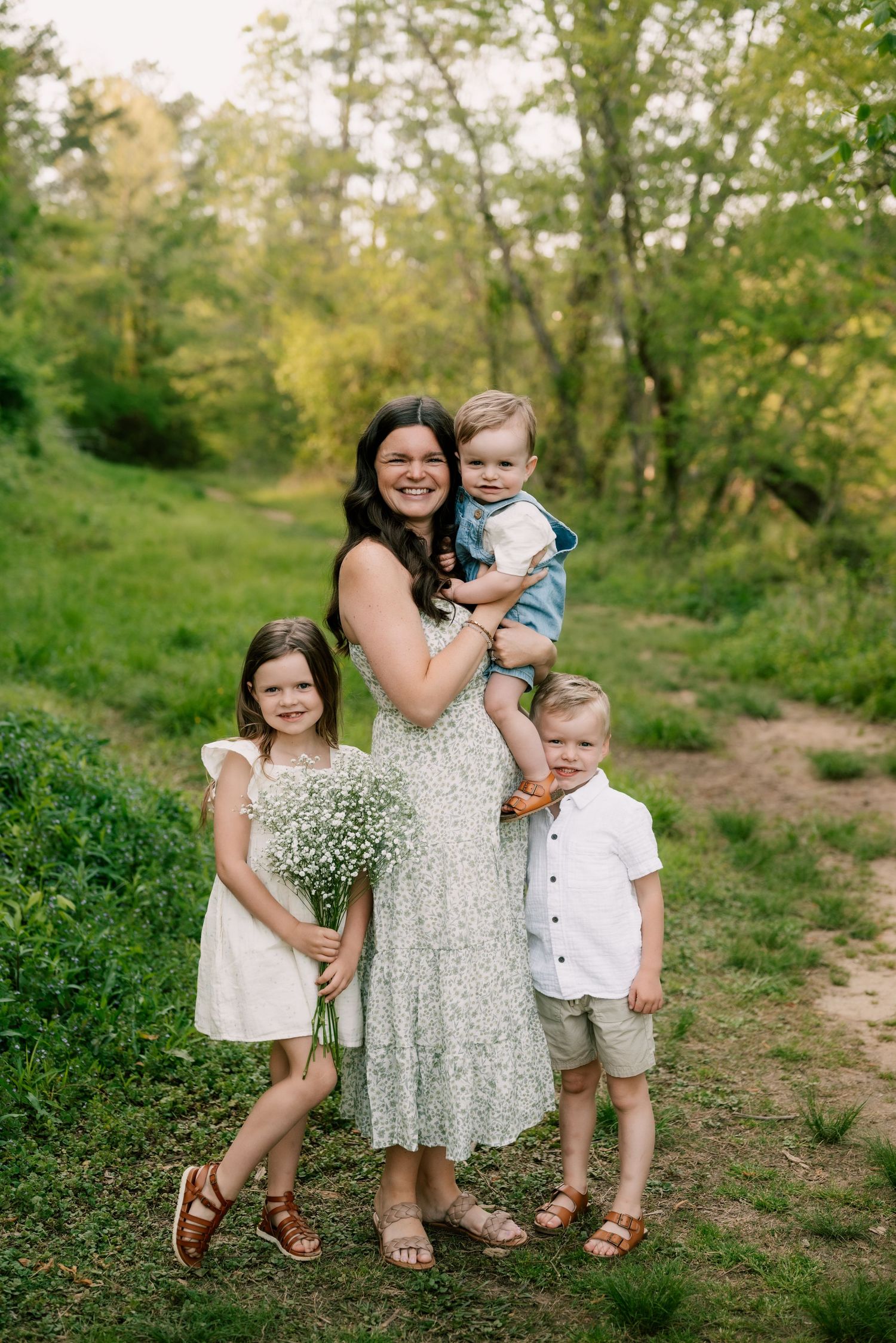 A mother and two children pose together for springtime family photos in a lush green outdoor setting.
