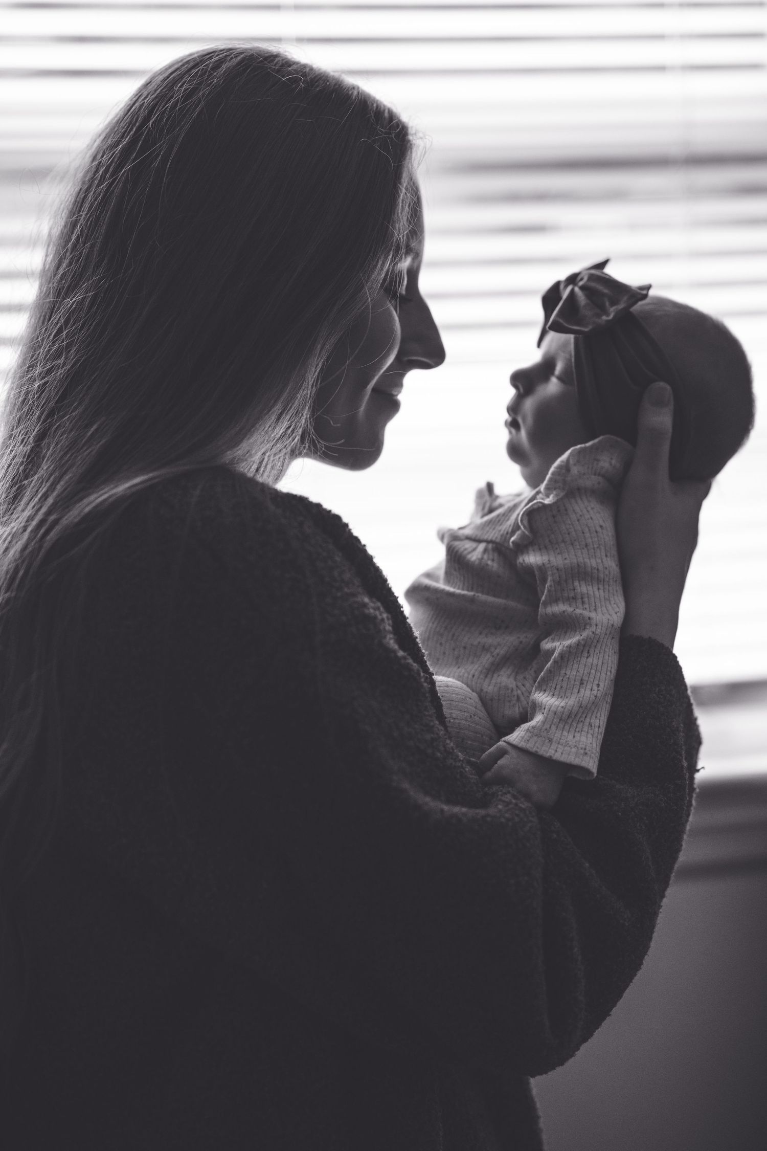 Silhouette portrait of parent holding baby against window light.
