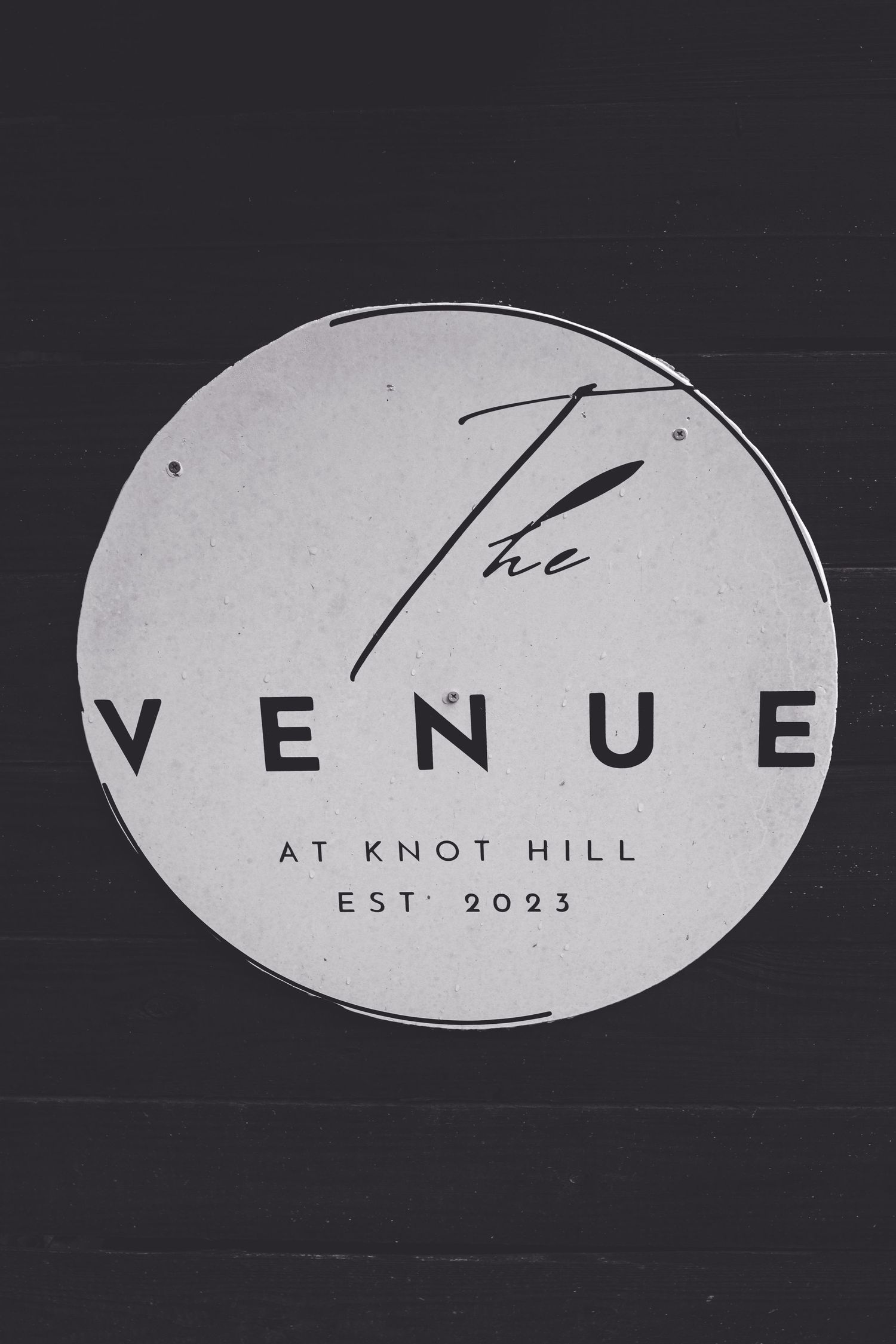 Circular sign for The Venue at Knot Hill, established 2023, mounted on dark wood wall.