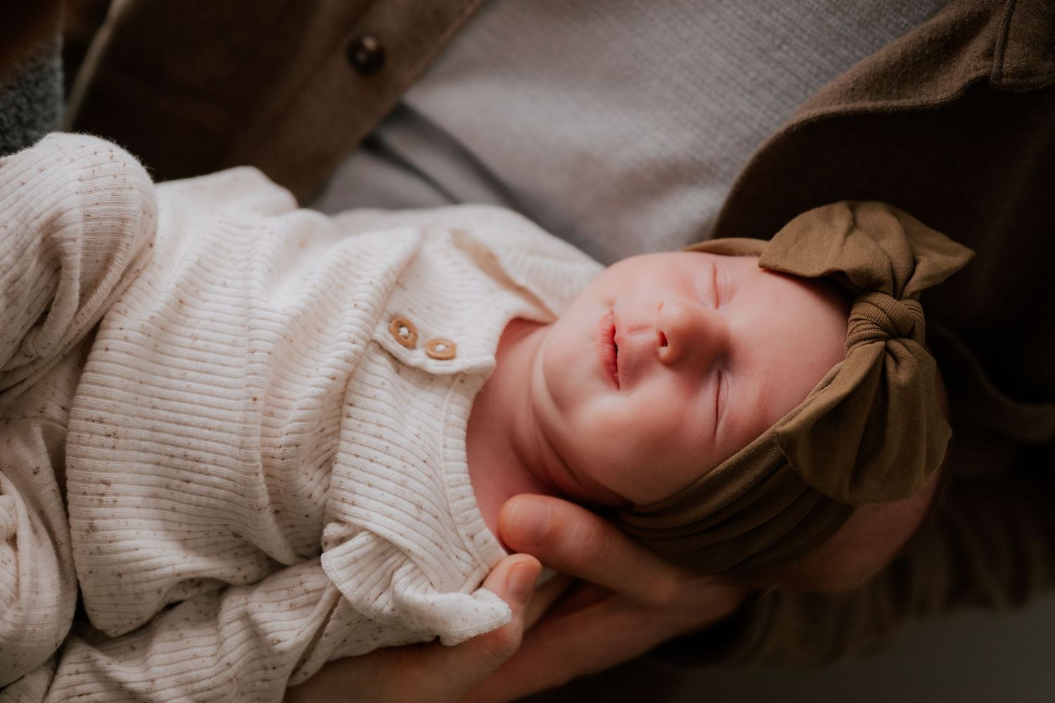 A sleeping baby wearing a white cardigan rests peacefully on soft fabric.