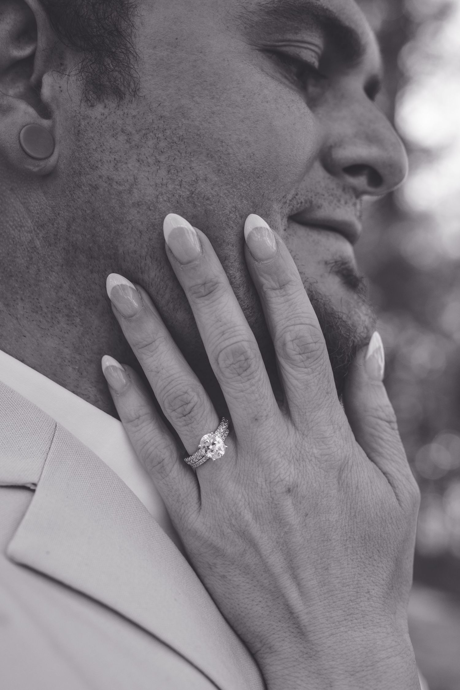 Close-up black and white photo showing a hand wearing almond-shaped acrylic nails and a sparkly engagement ring.