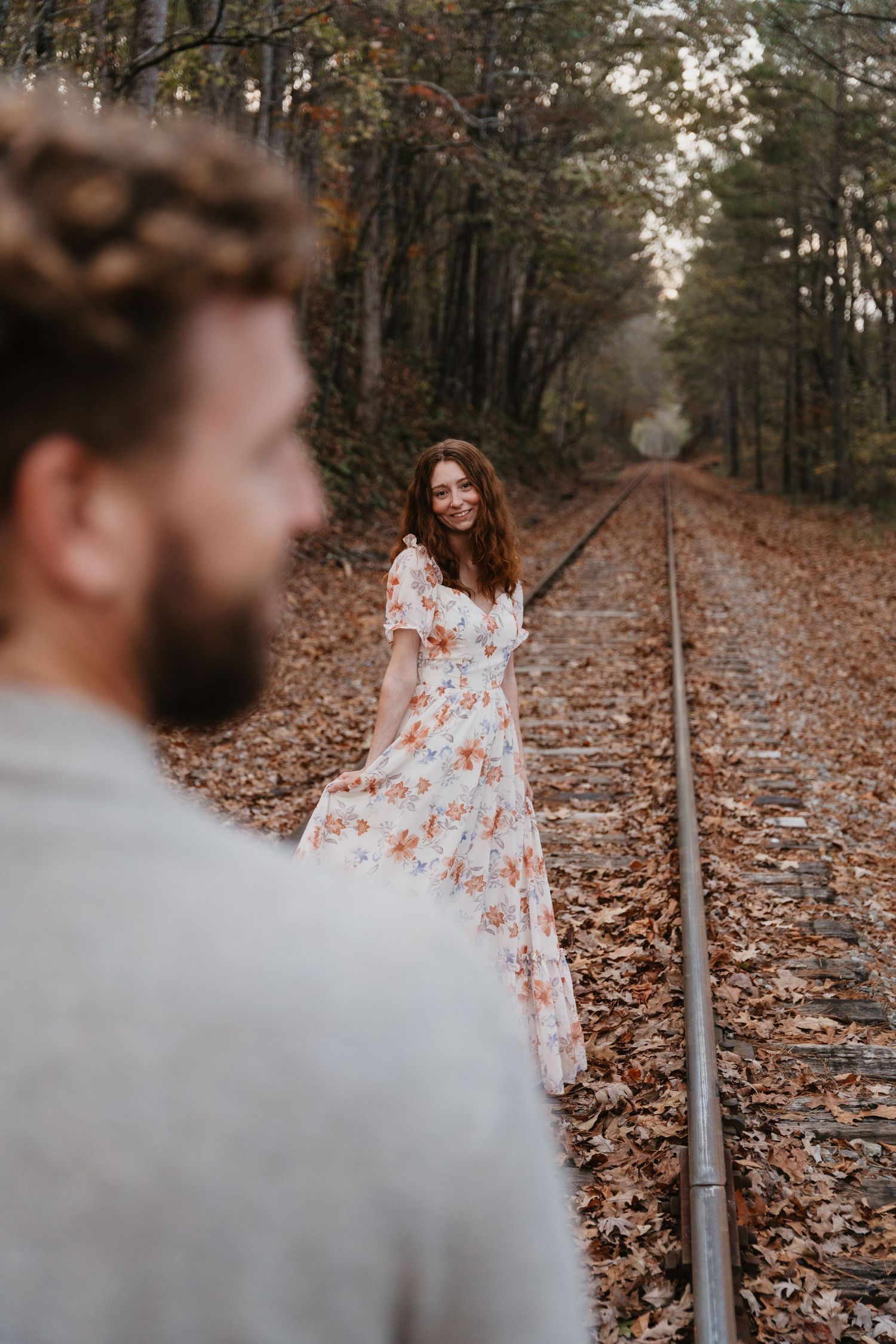 A romantic autumn photoshoot on train tracks with fallen leaves as a floral dress catches the light through the trees. Southern Pines,NC
