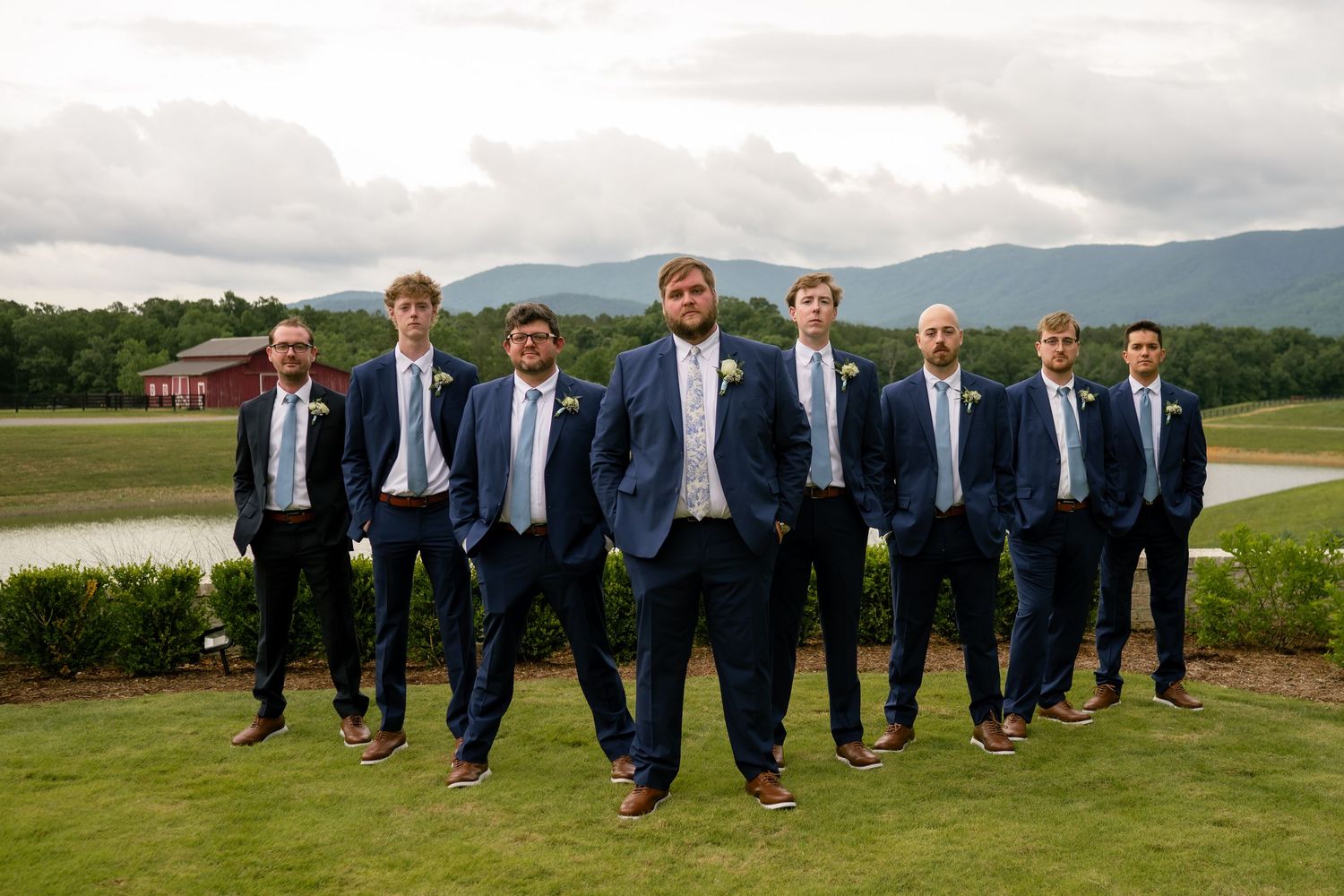 Groomsmen in navy suits with light blue ties pose outdoors at a wedding venue with mountain views.