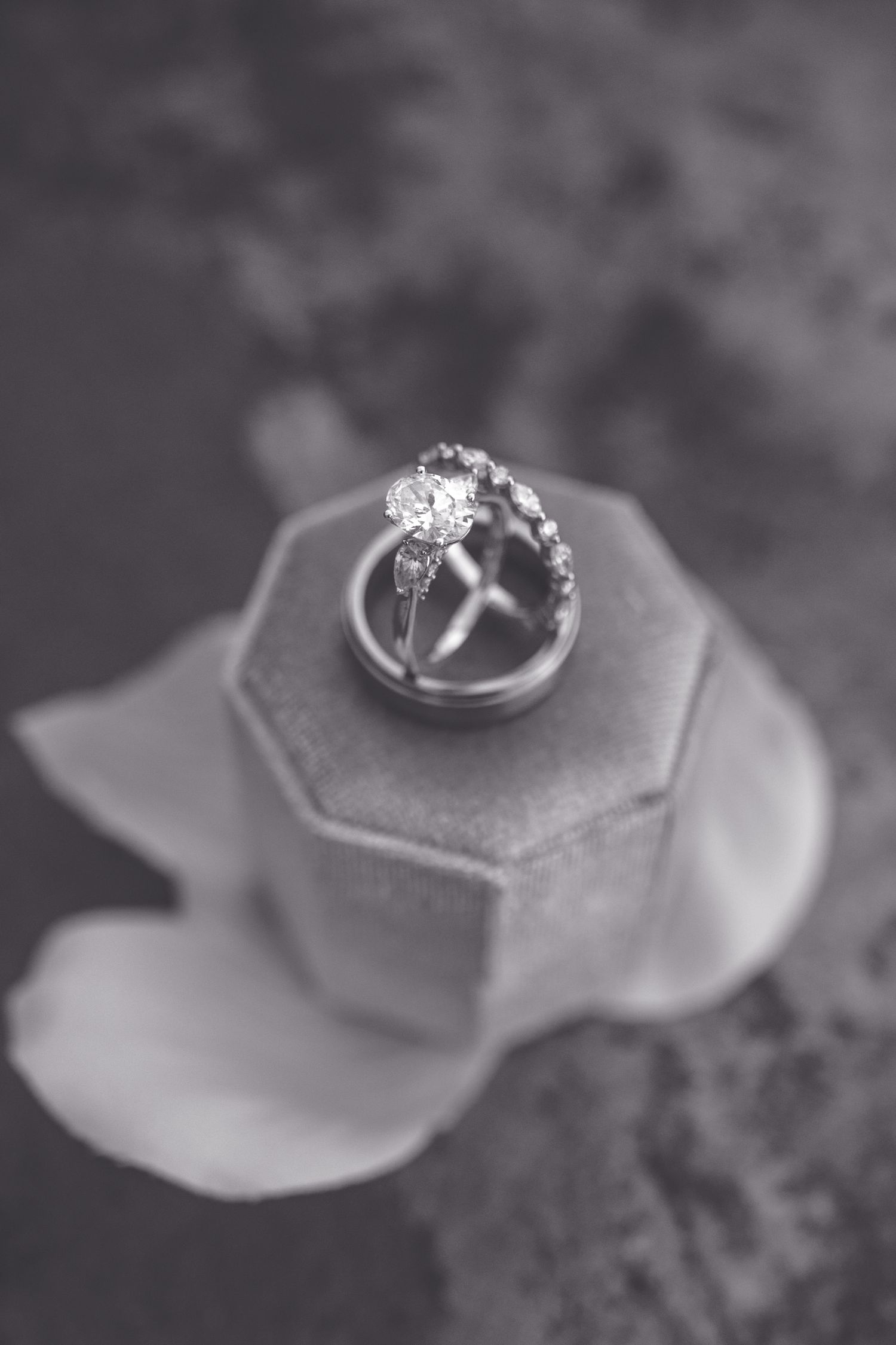 Black and white photo of diamond engagement ring and wedding bands displayed in an elegant hexagonal ring box with floral detail.