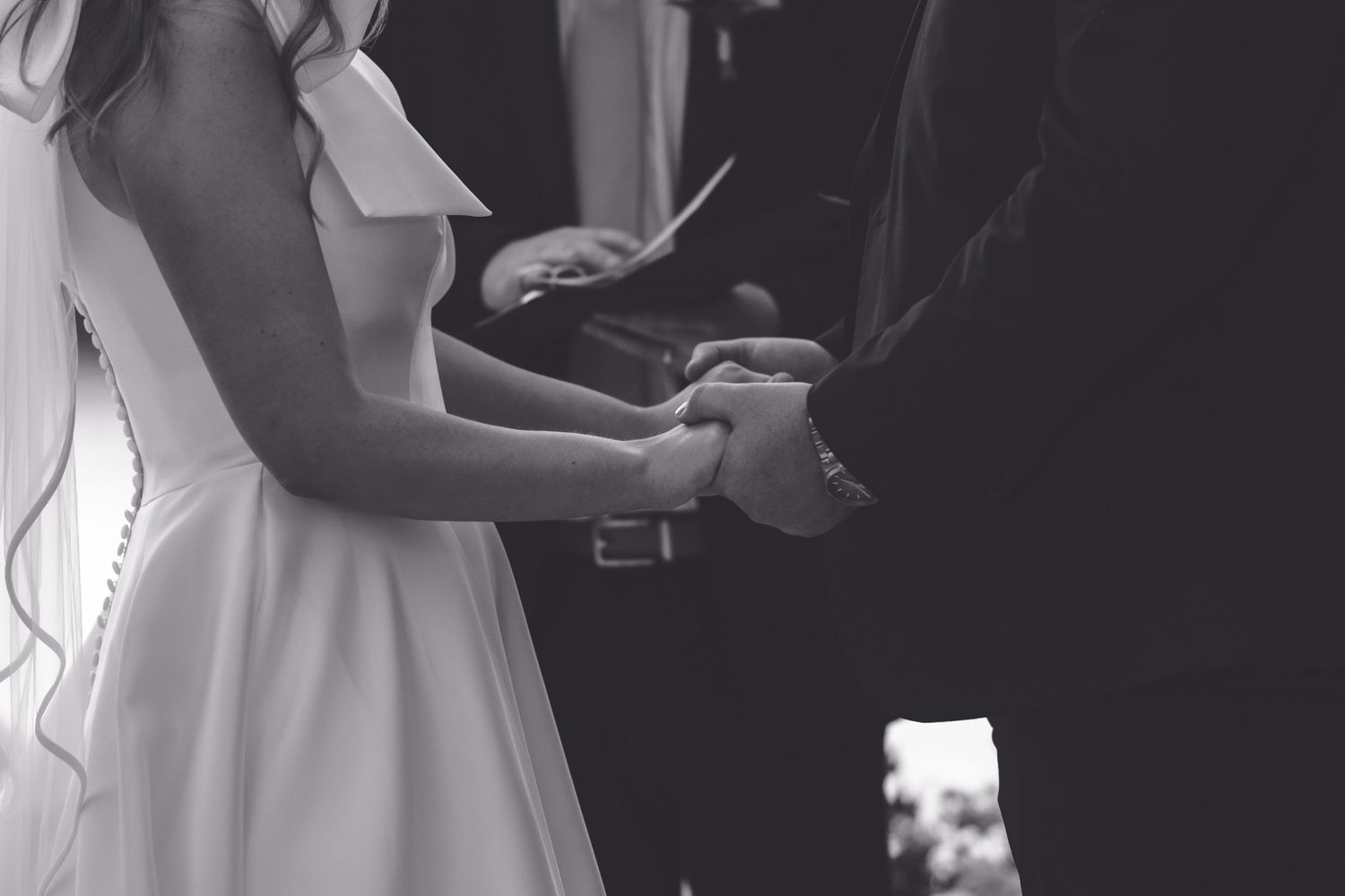 Black and white photo of bride and groom holding hands during wedding ceremony.