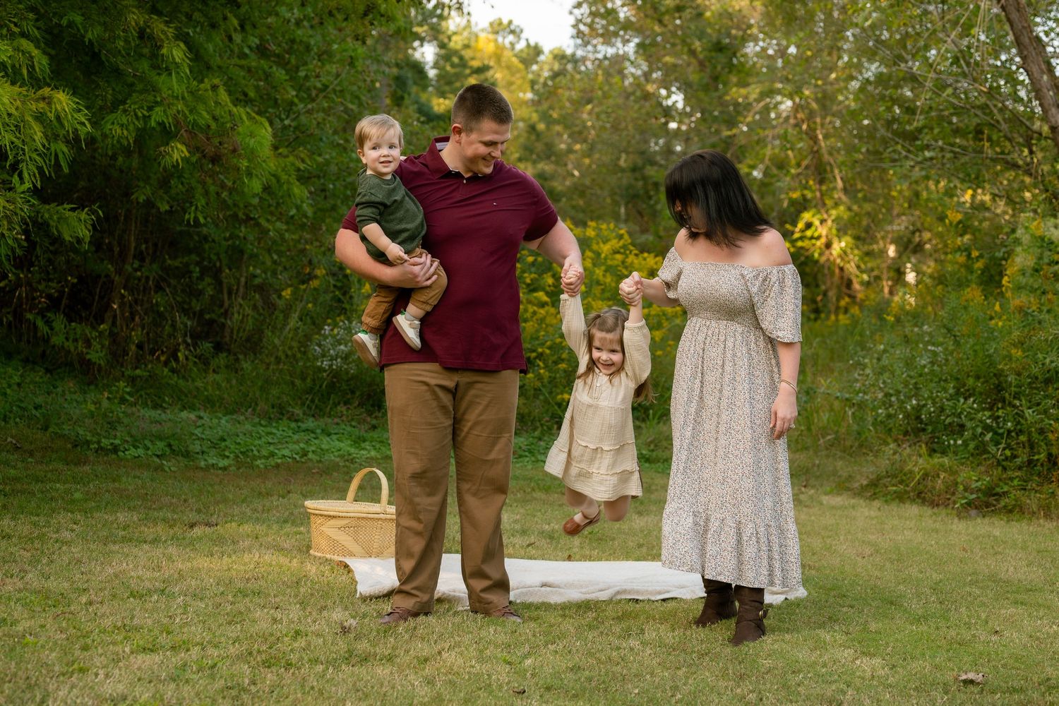 A group in burgundy and beige outfits walks together through a sunlit grassy area during golden hour.