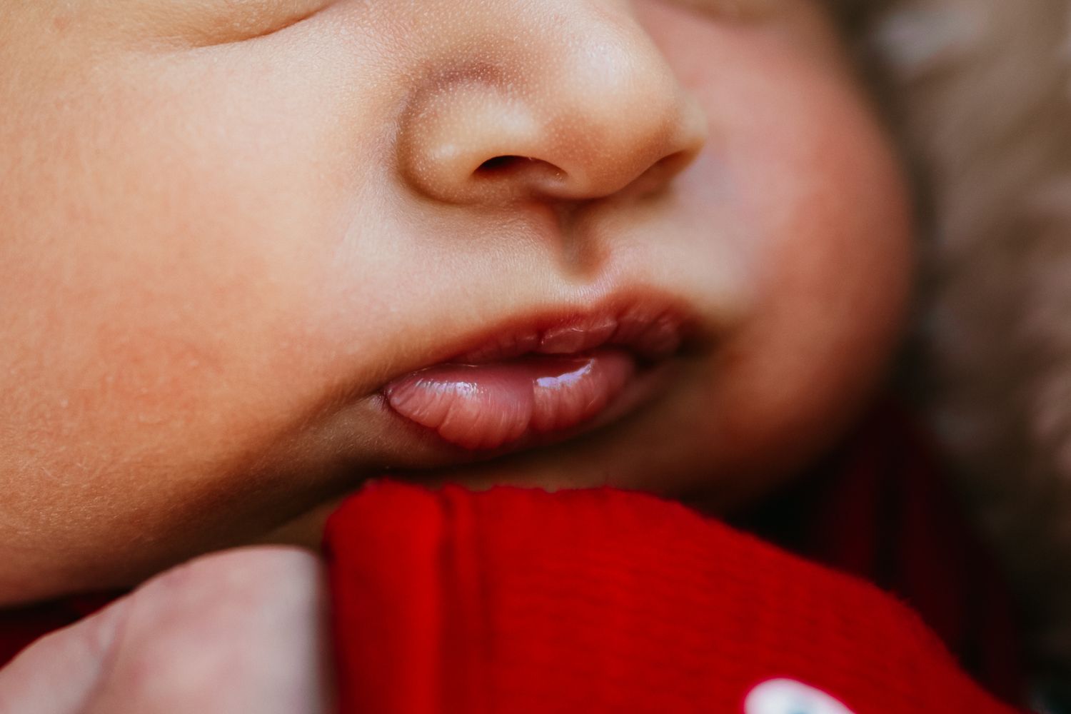 Close-up macro photo of soft baby lips and nose against a red fabric background.