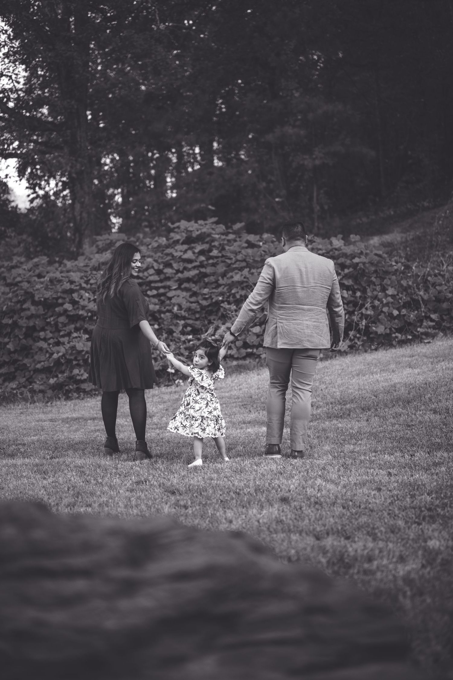 A black and white photo of a family walking together while holding hands on a grassy hill.