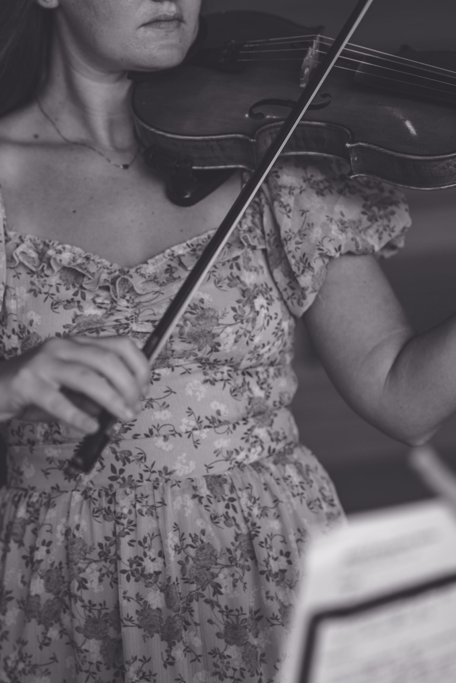 Woman in floral dress playing violin at wedding reception.