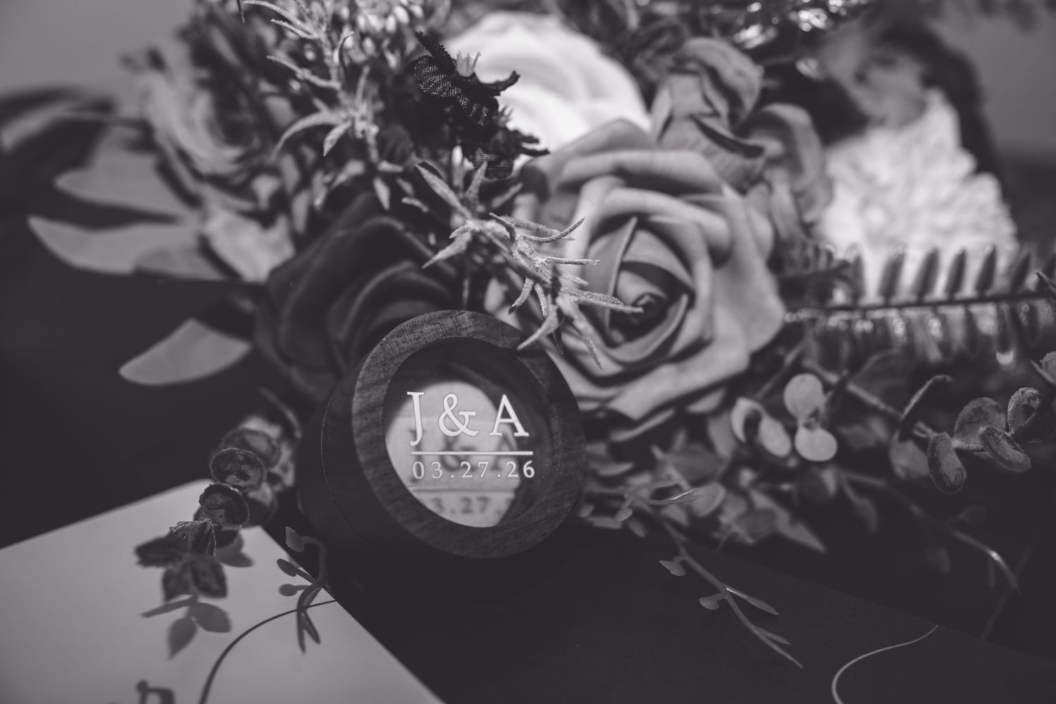Black and white wedding bouquet with roses and a personalized monogram charm engraved with I&A.