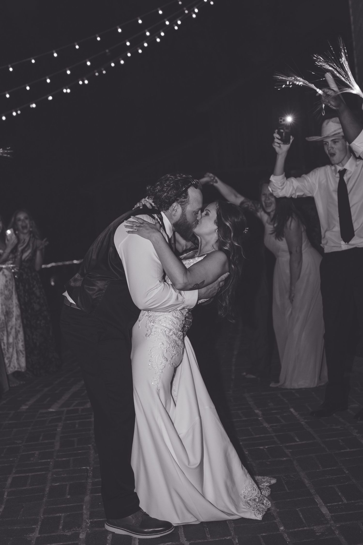 Black and white photo of bride and groom sharing a romantic kiss on the dance floor at night.